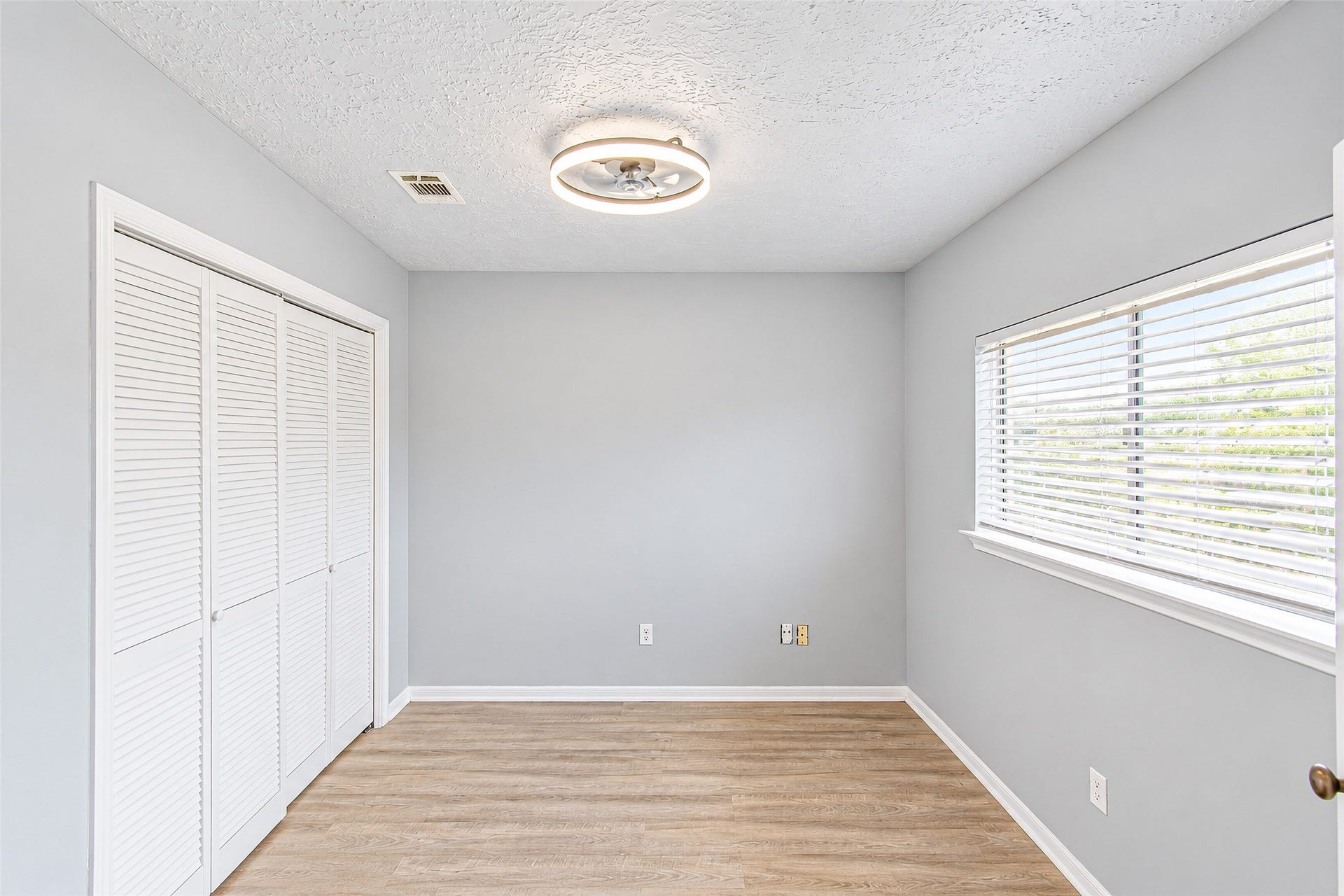 12027 Huntington Park Drive, Houston, TX 77099 Bright and airy room featuring light hardwood floors, a modern ceiling fixture, and ample closet space with white louvered doors.