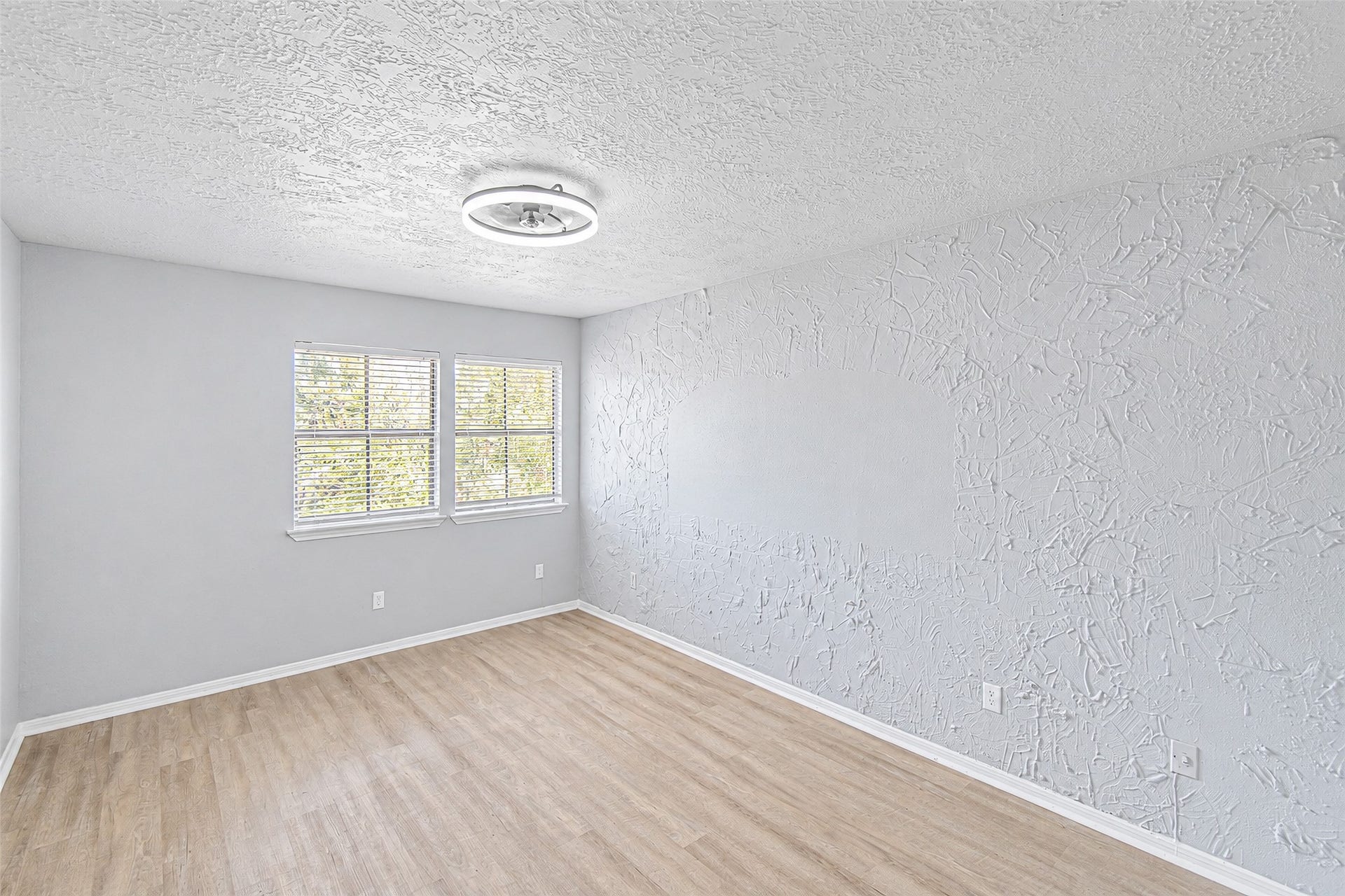 12027 Huntington Park Drive, Houston, TX 77099 Bright and airy room featuring textured walls, large windows for ample natural light, and elegant wood-look flooring.