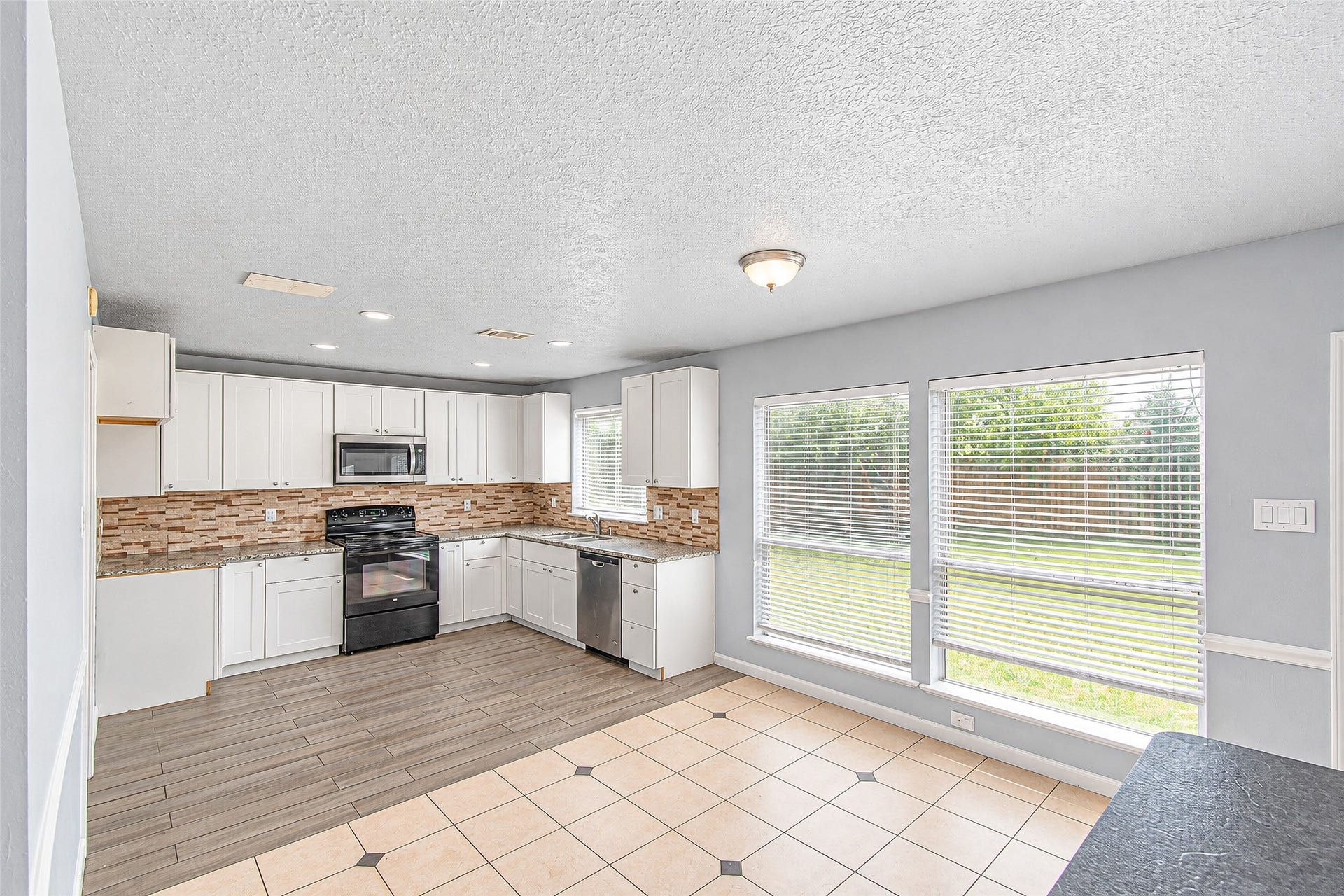 12027 Huntington Park Drive, Houston, TX 77099 Bright and spacious kitchen with modern white cabinetry, sleek black appliances, and a stylish tile backsplash. Large windows provide abundant natural light and a view of the backyard.