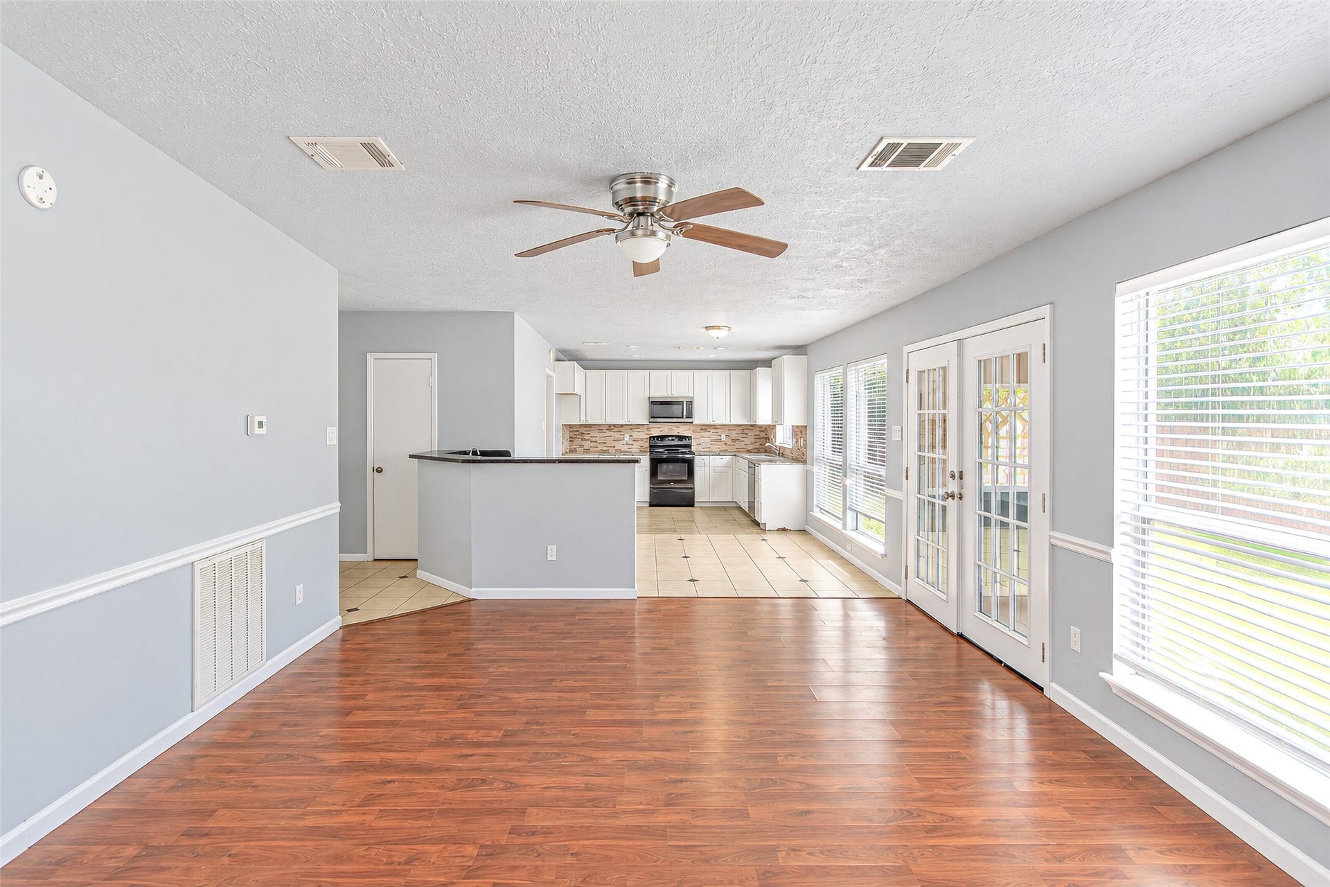 12027 Huntington Park Drive, Houston, TX 77099 Spacious open-concept living area with elegant wood flooring, abundant natural light through large windows and French doors, and a modern kitchen featuring sleek countertops and stainless steel appliances.