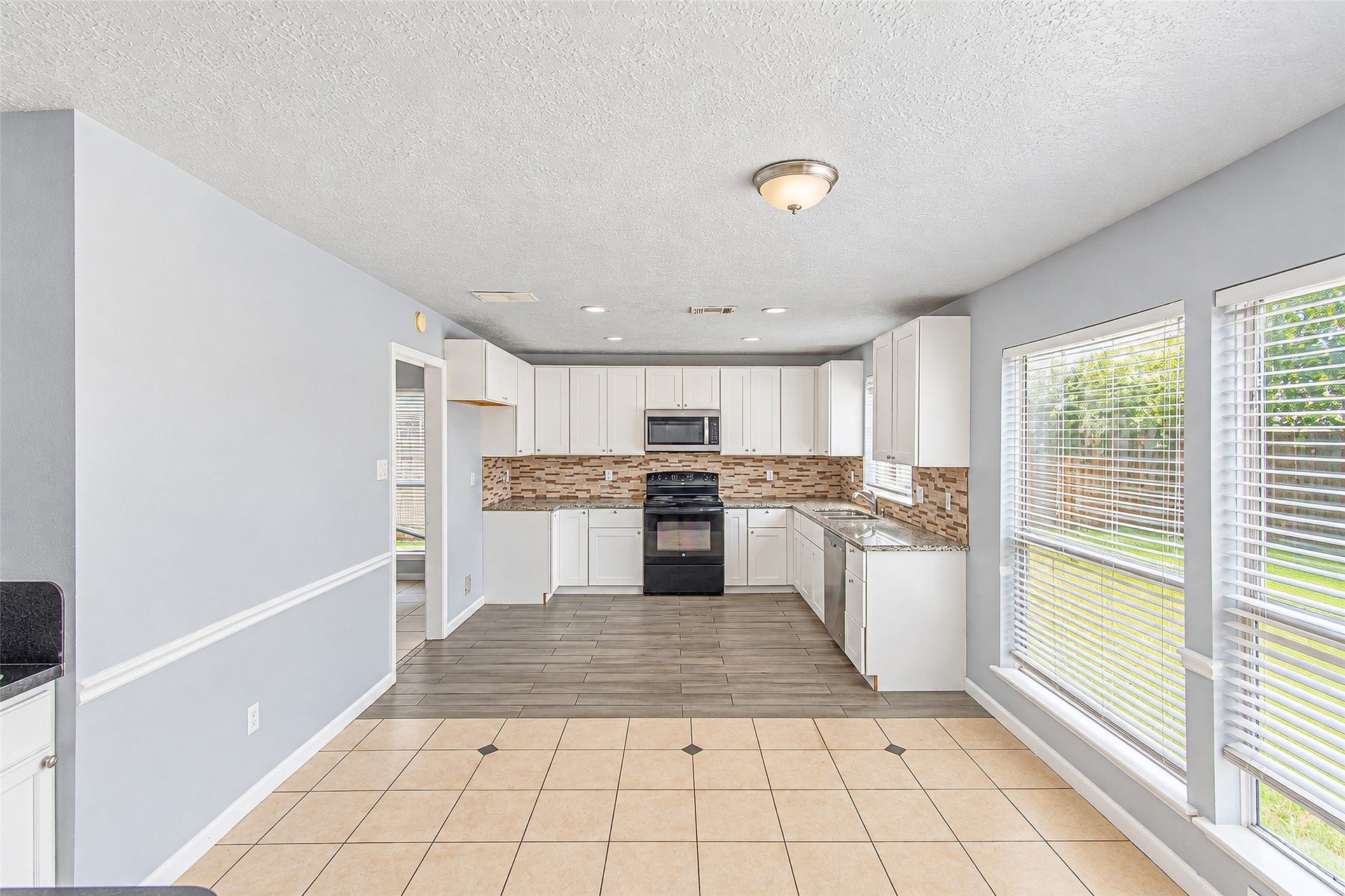 12027 Huntington Park Drive, Houston, TX 77099 Bright and inviting kitchen with sleek white cabinetry, modern black appliances, and a stylish tile backsplash. Large windows provide ample natural light, enhancing the open and spacious feel.