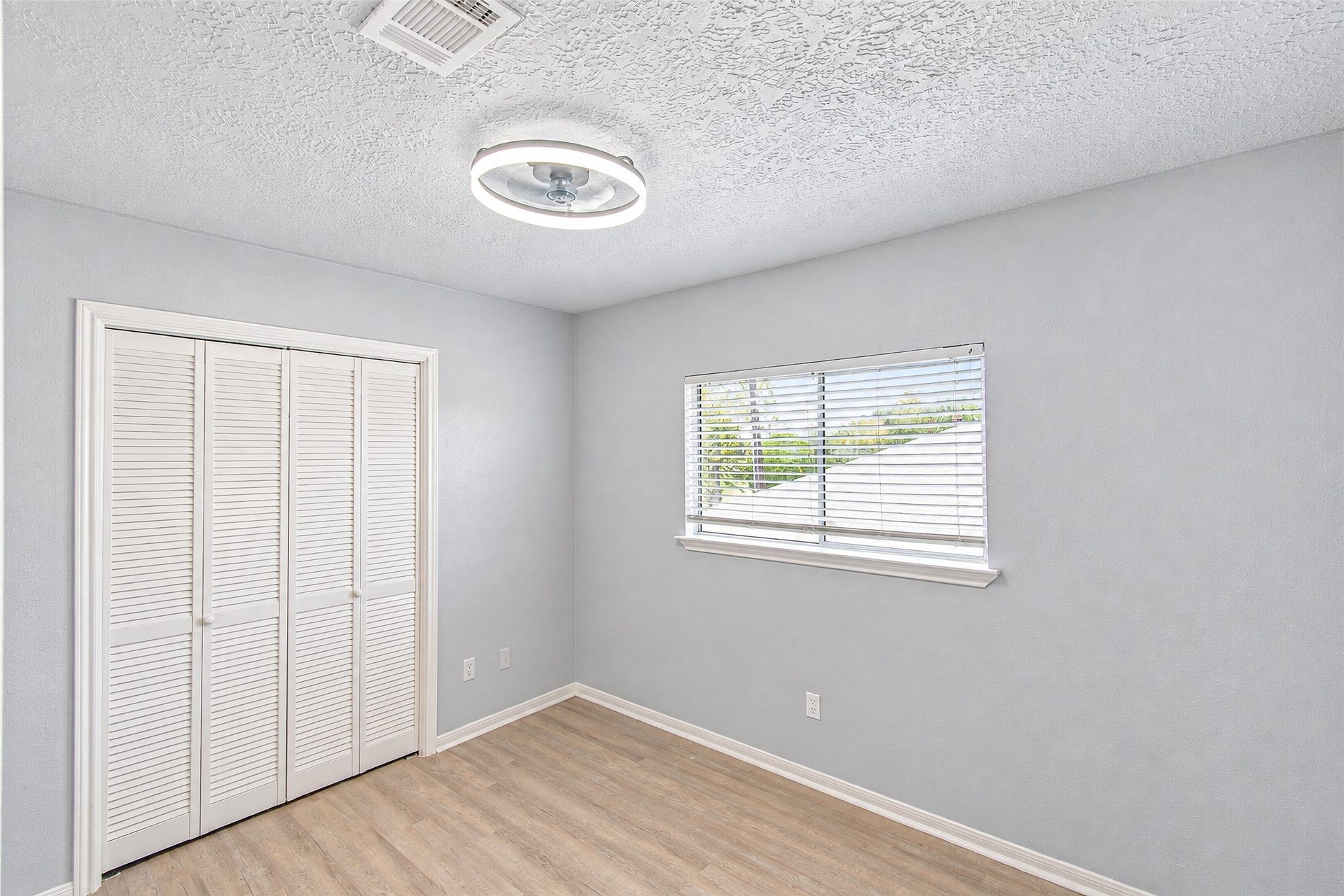 12027 Huntington Park Drive, Houston, TX 77099 Bright and airy room featuring a modern light fixture, light wood flooring, and a window with blinds, perfect for a cozy retreat.