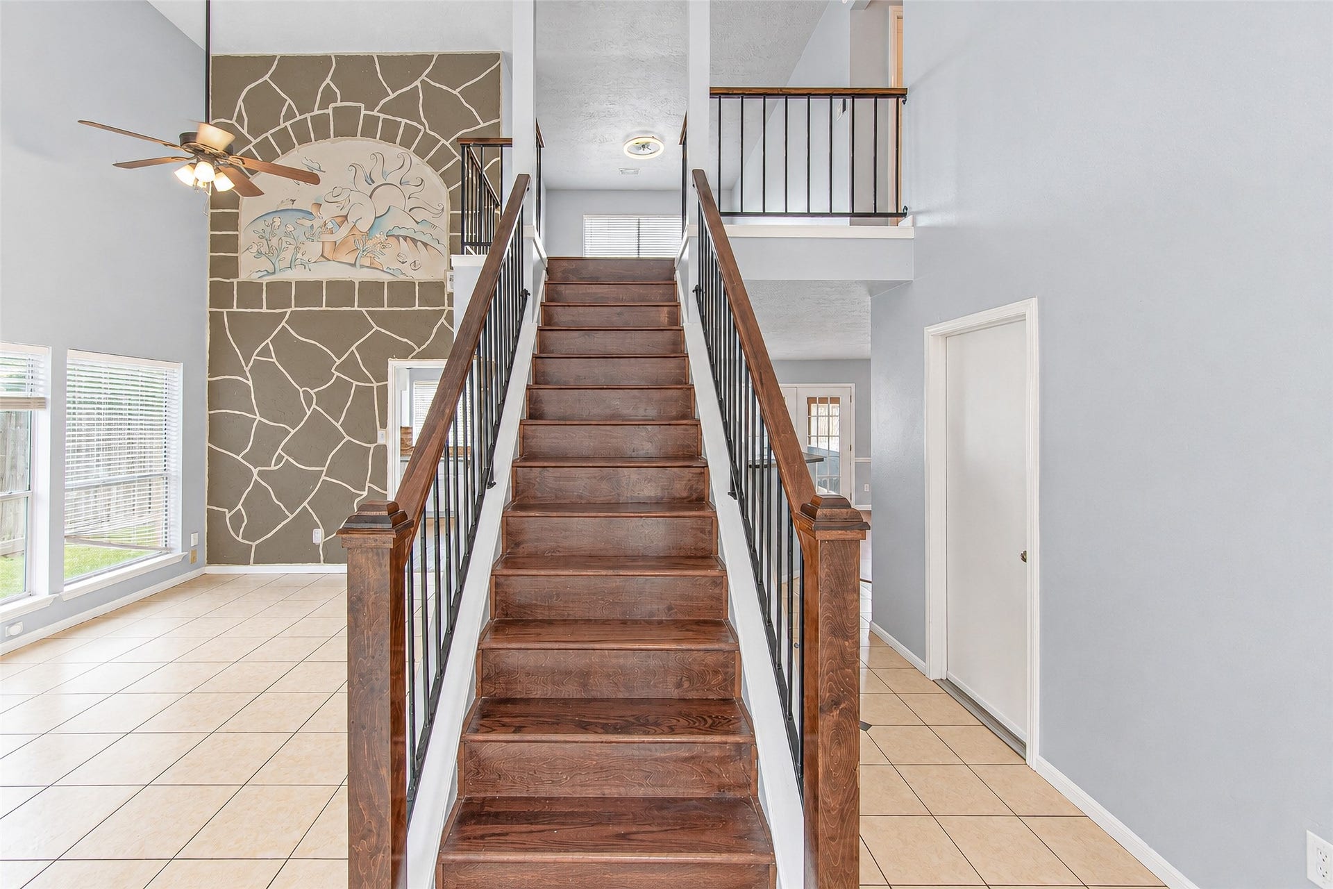 12027 Huntington Park Drive, Houston, TX 77099 Elegant foyer featuring a stunning wooden staircase with iron railings, leading to an airy loft space. The high ceiling and large windows fill the area with natural light, and a unique stone accent wall adds character.