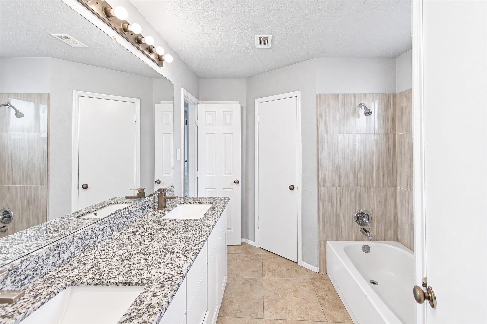 12027 Huntington Park Drive, Houston, TX 77099 Bright and modern bathroom featuring a sleek granite countertop with dual sinks, a full bathtub with stylish tile surround, and ample lighting.