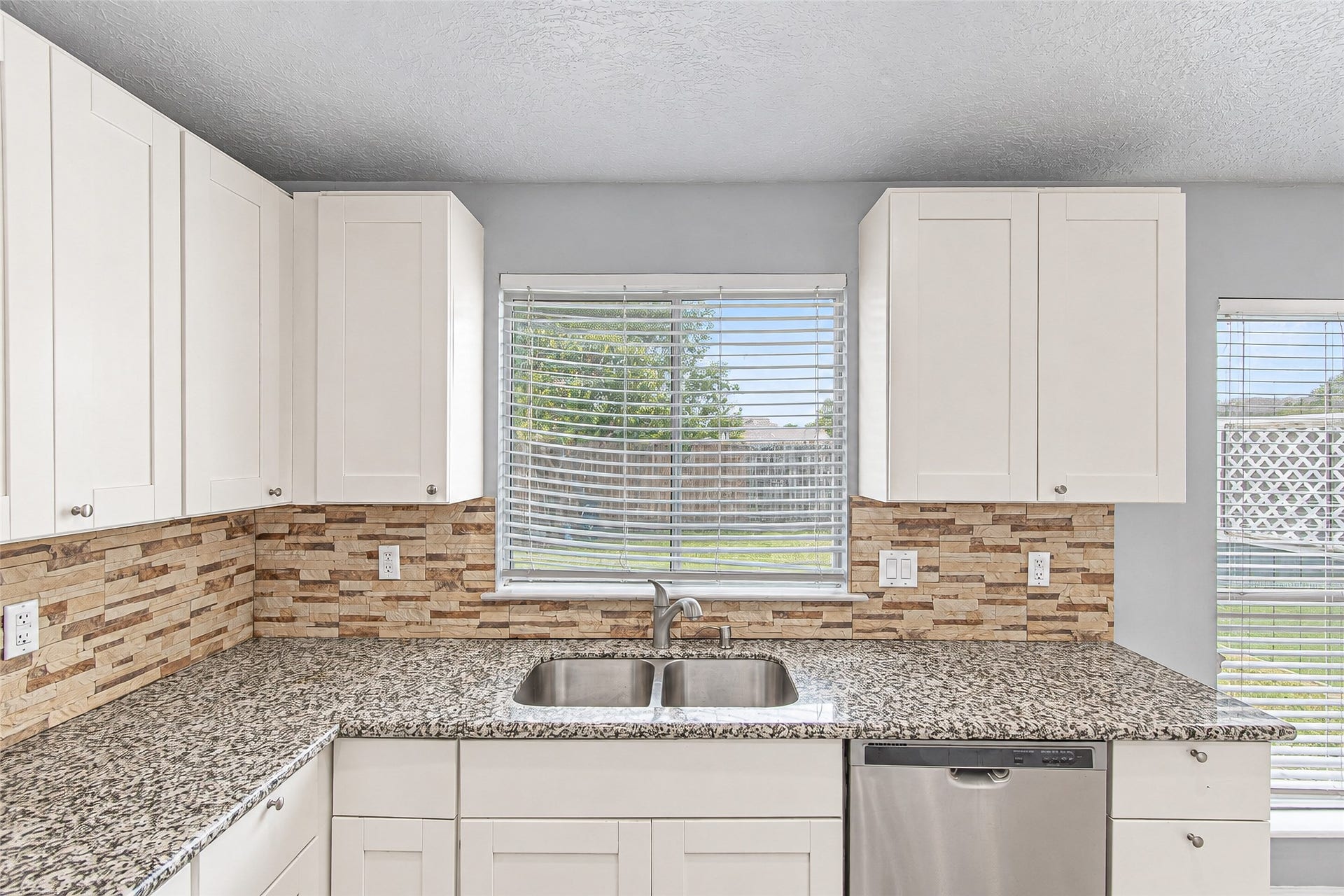 12027 Huntington Park Drive, Houston, TX 77099 Bright kitchen featuring sleek granite countertops, modern stainless steel appliances, and ample white cabinetry, complemented by a stylish tile backsplash and a window view.