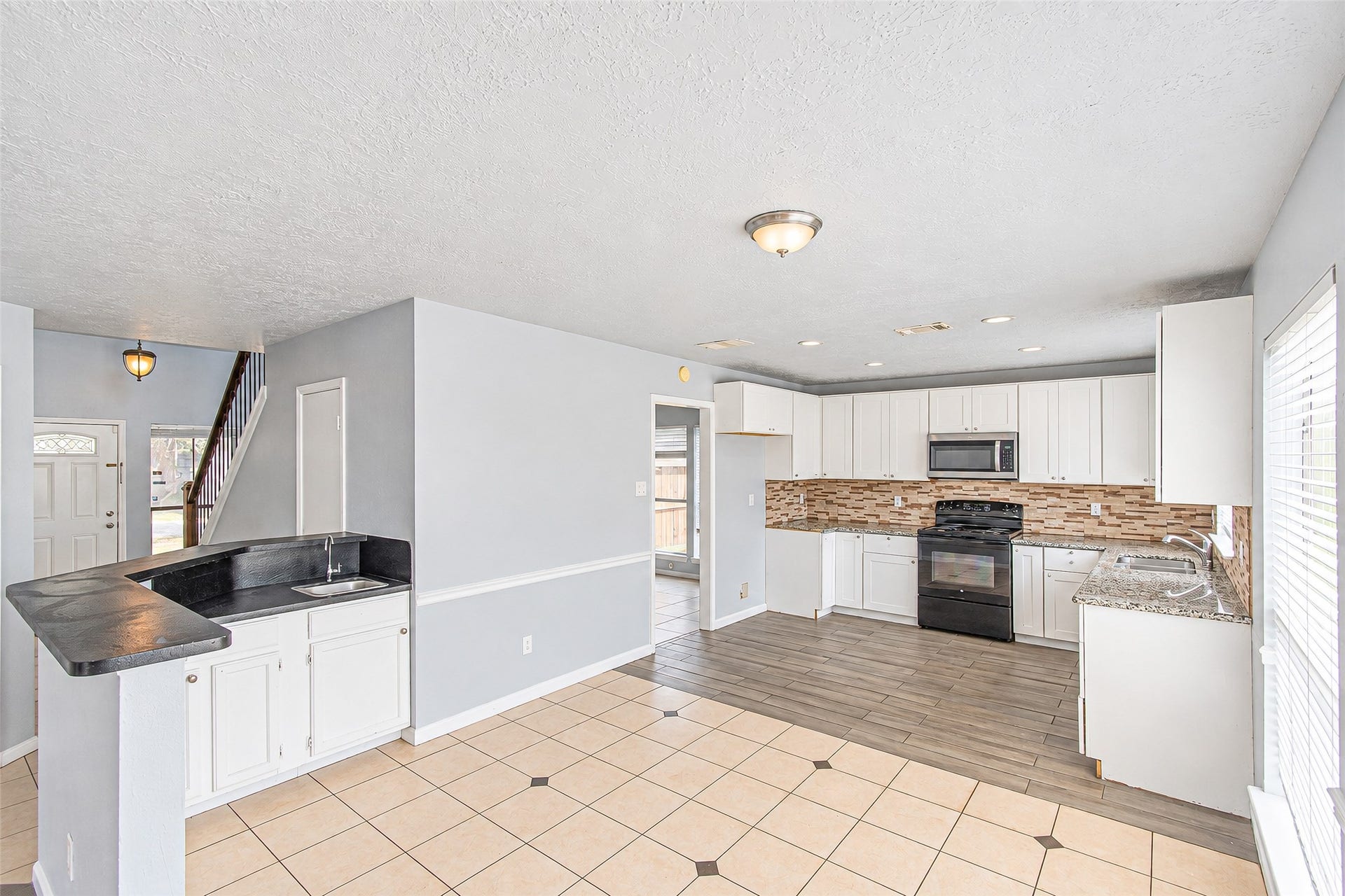 12027 Huntington Park Drive, Houston, TX 77099 Bright and spacious kitchen features modern white cabinetry, sleek countertops, and a stylish tile backsplash, seamlessly flowing into an open-concept living area with abundant natural light.