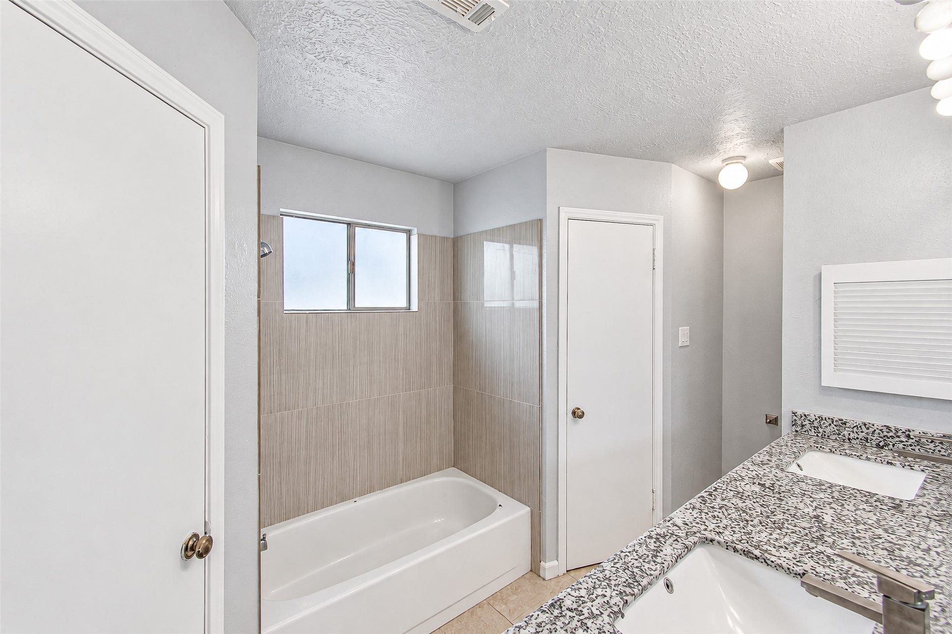 12027 Huntington Park Drive, Houston, TX 77099 Bright and modern bathroom featuring a sleek granite countertop with dual sinks, a tiled bathtub, and ample lighting.