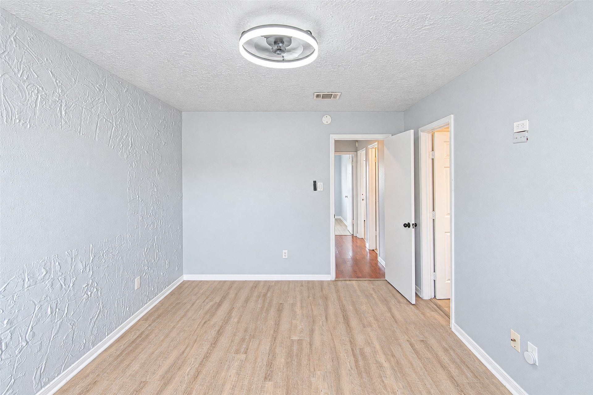 12027 Huntington Park Drive, Houston, TX 77099 Bright room with textured walls and wood-like flooring, featuring a modern ceiling light and access to adjoining spaces through white doors.