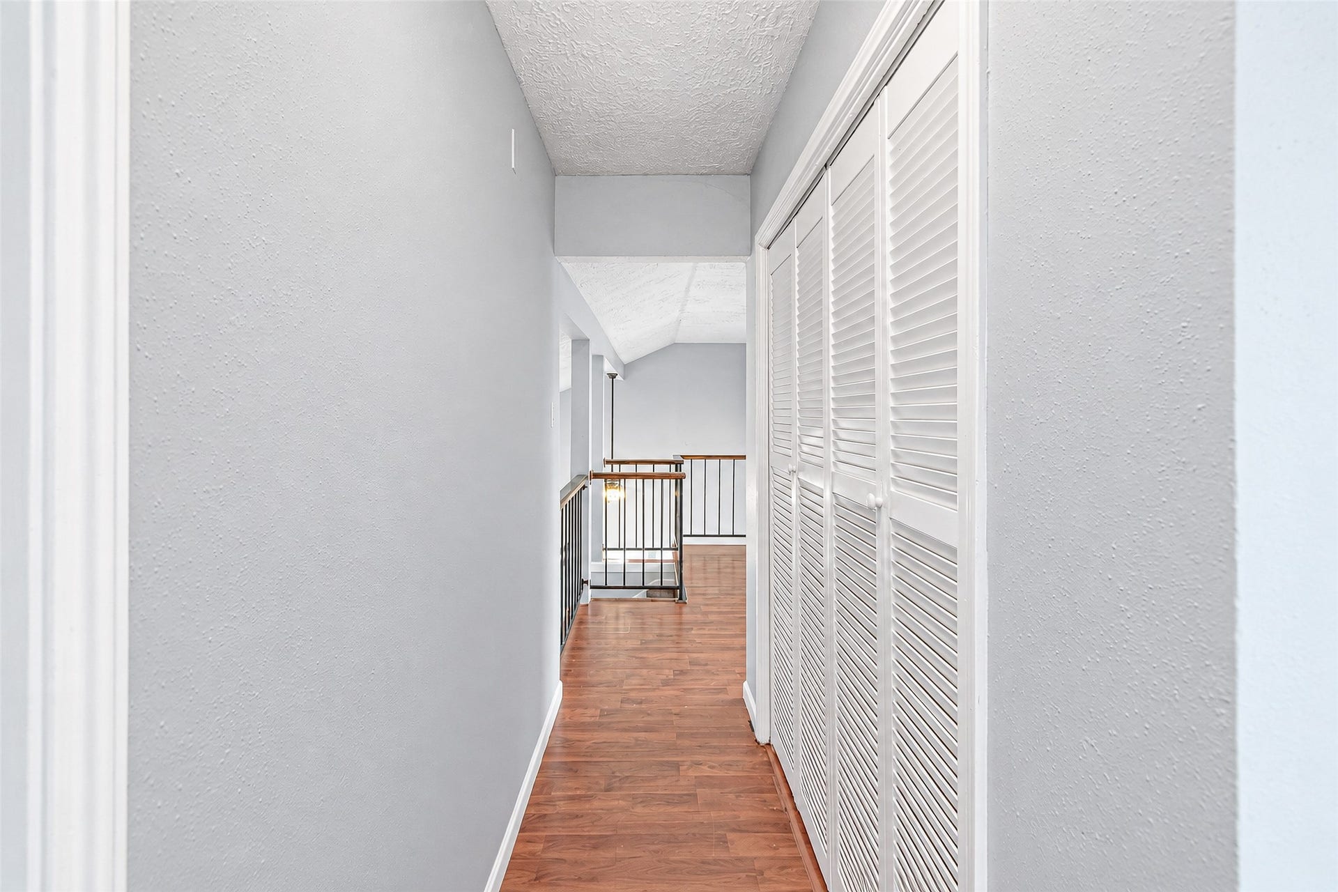 12027 Huntington Park Drive, Houston, TX 77099 Bright hallway with elegant wood flooring and ample closet space, leading to an airy open railing overlooking the living area.