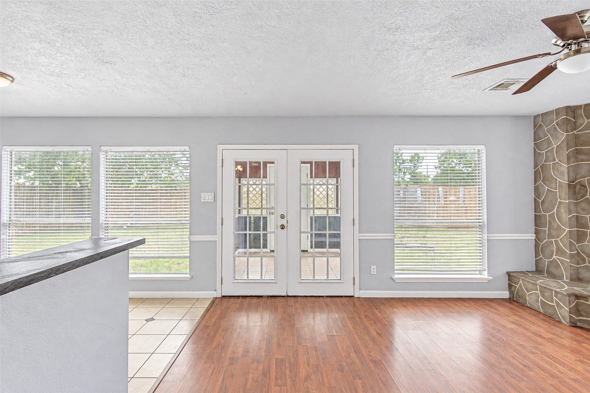 12027 Huntington Park Drive, Houston, TX 77099 Bright living space with hardwood floors, large windows, and French doors opening to the backyard, featuring a unique stone accent wall and ceiling fan.