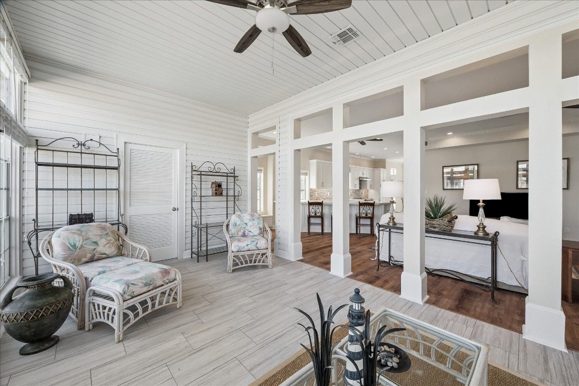 This photo showcases a bright and airy sunroom with wicker furniture and tiled flooring, seamlessly connecting to an open-concept living area with warm wood floors and a modern kitchen. The space is inviting and perfect for relaxation and entertaining.