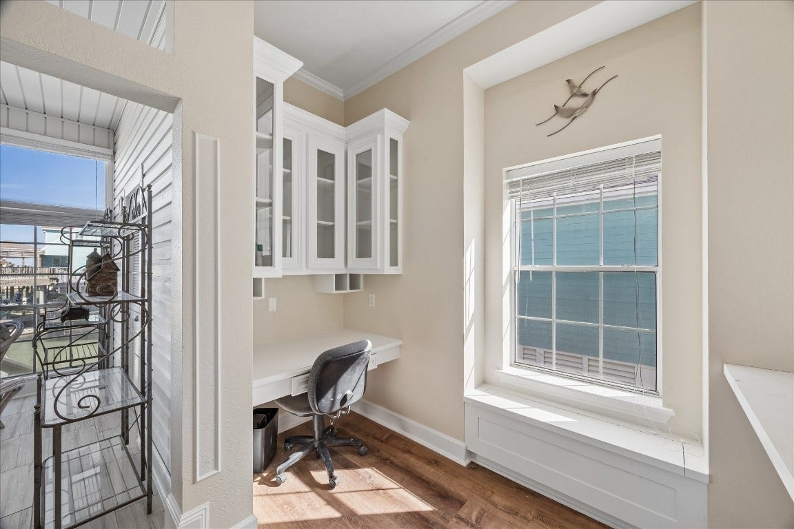 This bright, cozy office nook features a built-in desk with overhead storage cabinets, a window seat, and large windows for natural light. Ideal for working from home.