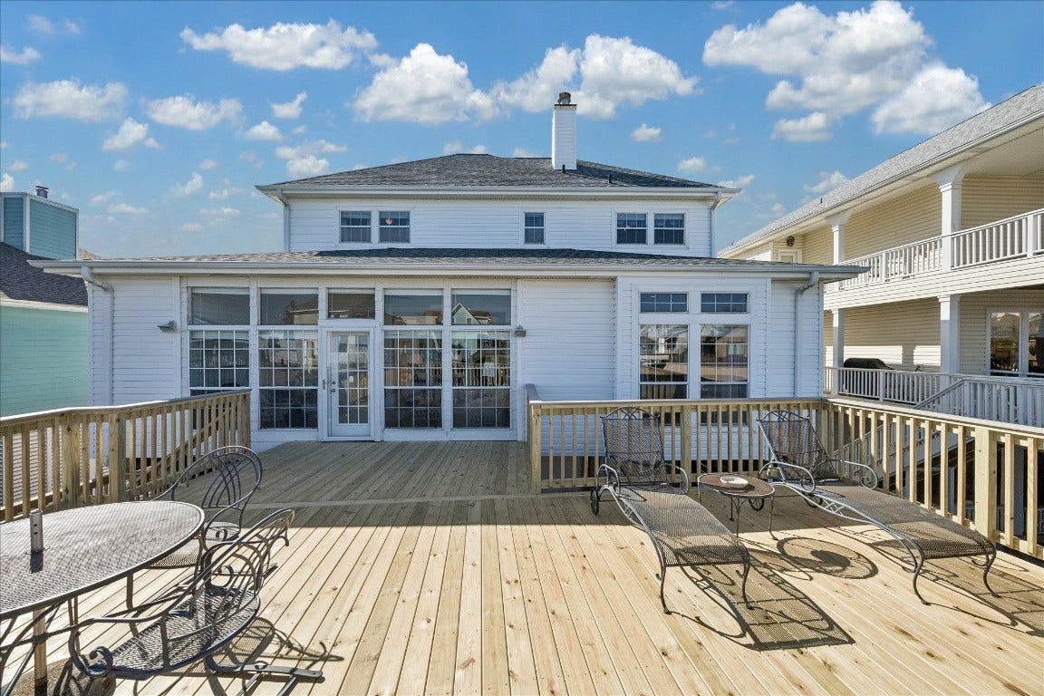 This photo showcases a spacious two-story home with a large wooden deck, perfect for outdoor lounging and entertaining. The house features multiple windows, allowing for plenty of natural light, and has a modern, clean exterior.