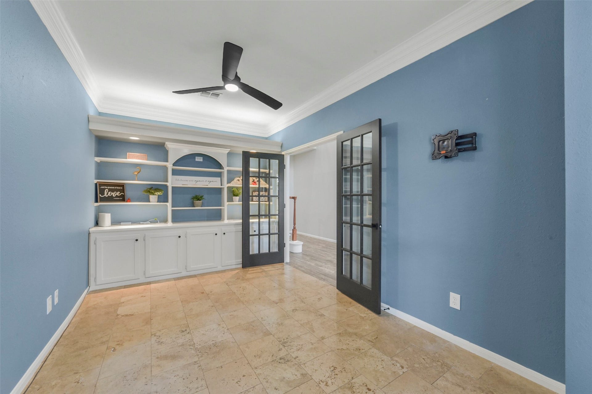 15730 Lake Loop Drive, Cypress, TX 77433 Elegant office featuring a built-in shelving unit, stylish French doors, and a modern ceiling fan, all set against soothing blue walls.