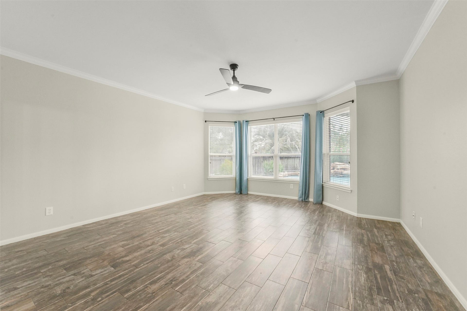 15730 Lake Loop Drive, Cypress, TX 77433 Spacious primary bedroom with elegant wood-look tile flooring, abundant natural light from large windows, and a sleek ceiling fan for comfort.
