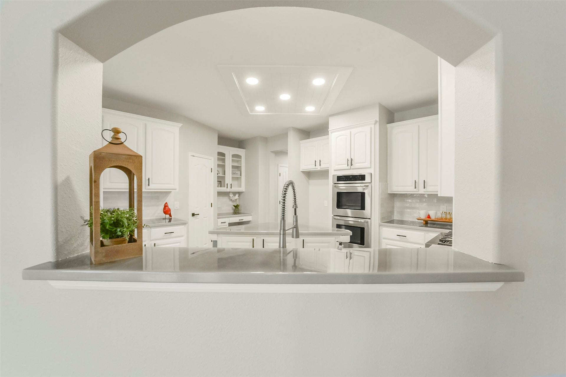 15730 Lake Loop Drive, Cypress, TX 77433 Elegant kitchen featuring modern stainless steel appliances, pristine white cabinetry, and a sleek arched pass-through for effortless entertaining.