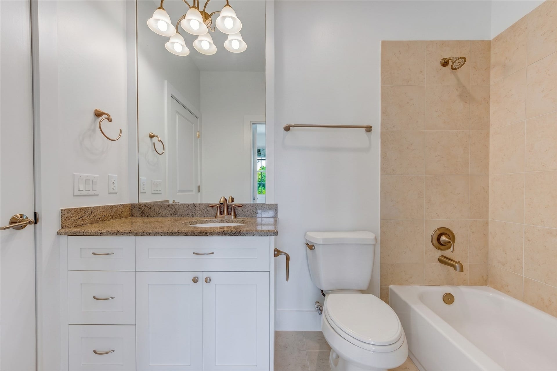 Private en-suite bath for the second upstairs secondary bedroom, featuring granite-topped vanity and tiled tub and shower combination.