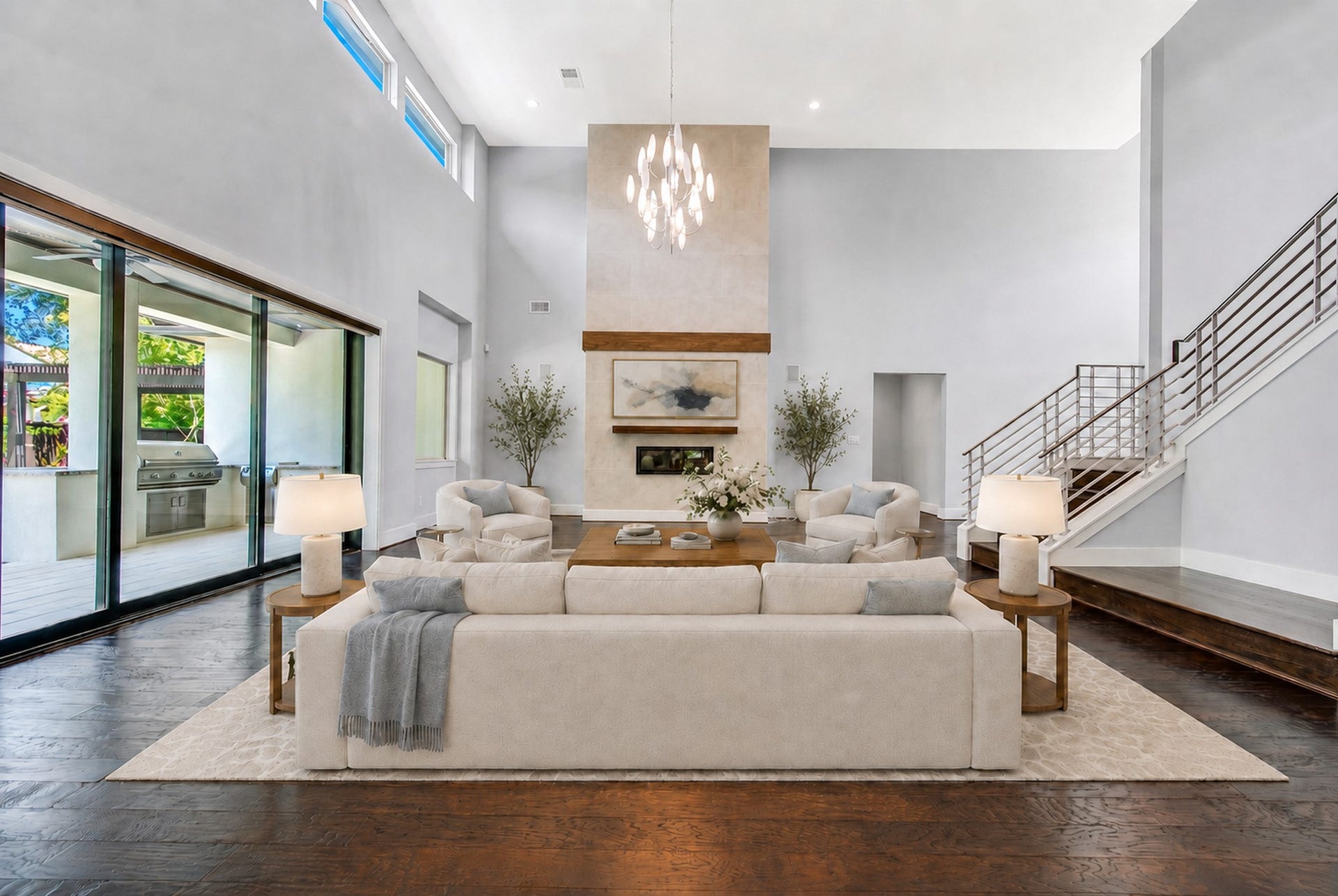 Soaring ceilings and sculptural lighting elevate the great room, where a dramatic floor-to-ceiling fireplace creates a striking architectural focal point. Digitally staged.