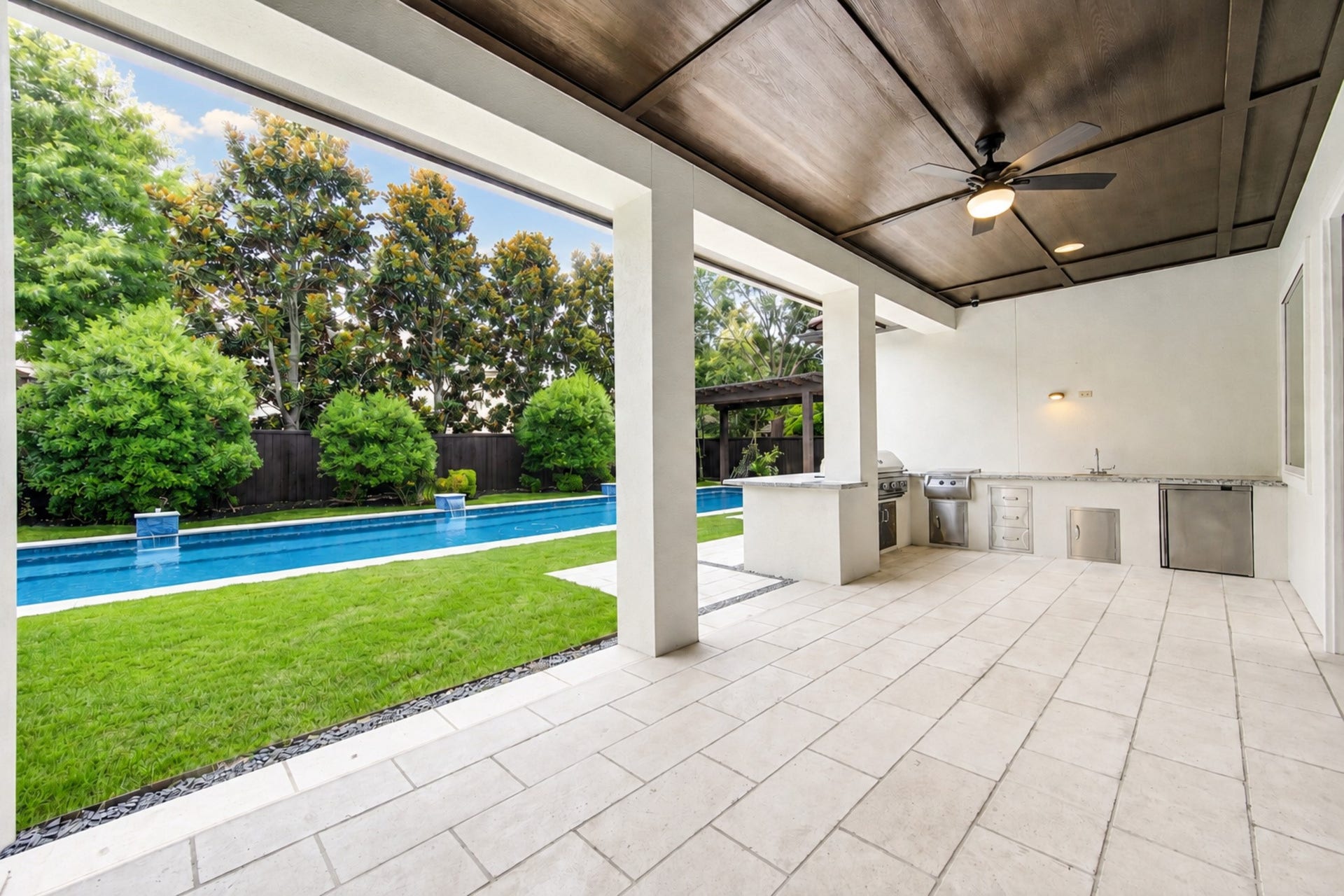 The expansive covered patio features a well-appointed outdoor kitchen and pool views, making alfresco dining and entertaining effortless year-round.
