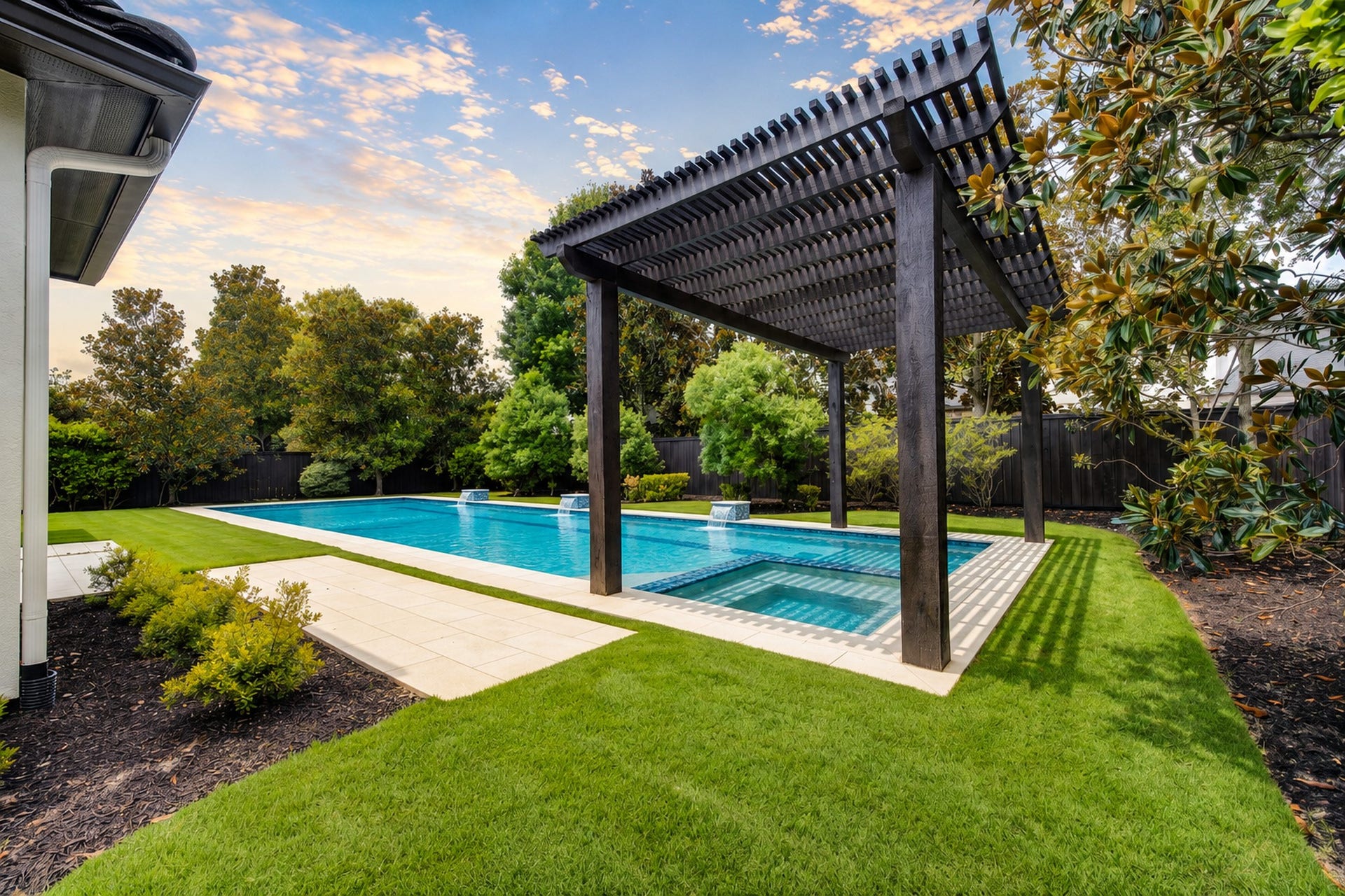 Lush landscaping surrounds the resort-style pool, where cascading water features and a dramatic pergola create a serene private escape.