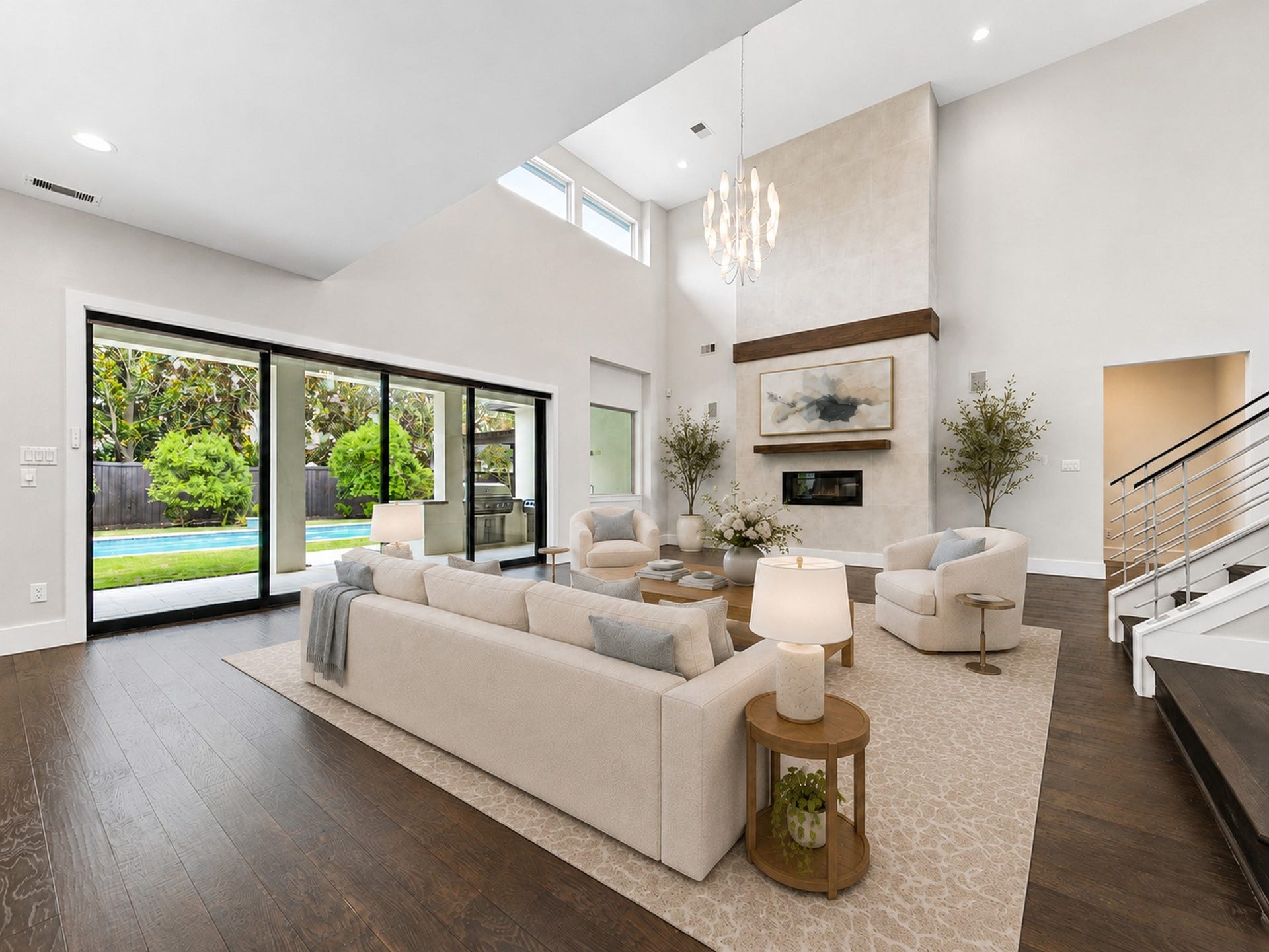 The spectacular two-story great room centers around a sleek fireplace, while walls of sliding doors open to serene pool views. Digitally staged.