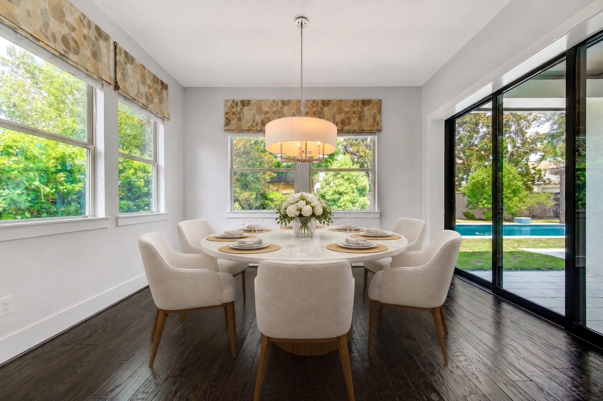 The sun-filled breakfast room enjoys panoramic pool and garden views, with sliding glass doors creating an effortless connection to the covered patio. Digitally staged.