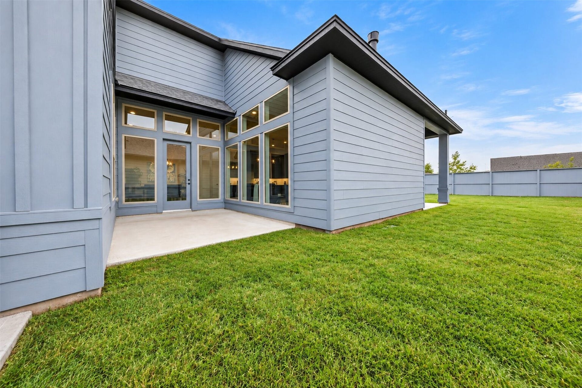 32510 Ebony Jewelwing Court, Fulshear, TX 77441 Backyard & Patio Rear exterior view showcasing the homes modern architecture, expansive windows, patio space, and grassy fenced yard.