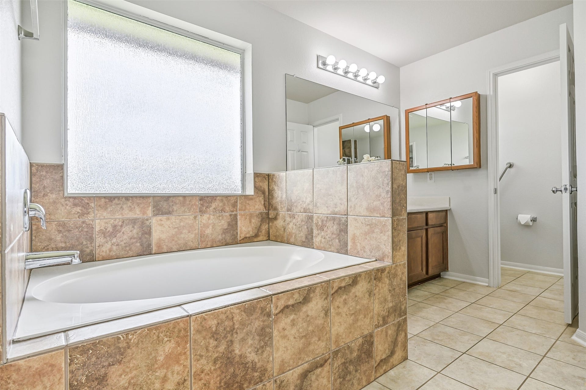 318 Lake Line Drive, Alvin, TX 77511 The spacious primary bath features a large tile-surround soaking tub beneath a privacy window, tile flooring and plenty of natural light, with the dual-sink vanity and separate shower completing the functional layout.