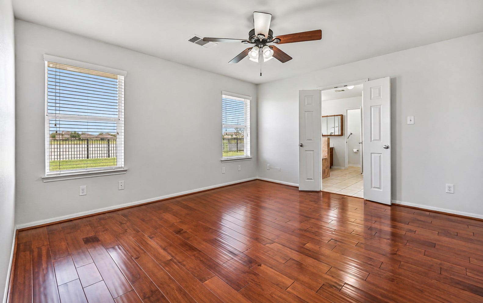 318 Lake Line Drive, Alvin, TX 77511 The secluded primary suite offers a peaceful retreat with rich wood flooring, fresh neutral paint, ceiling fan & two large windows framing views of the backyard and pond, while double doors lead directly into the spacious en-suite bath.