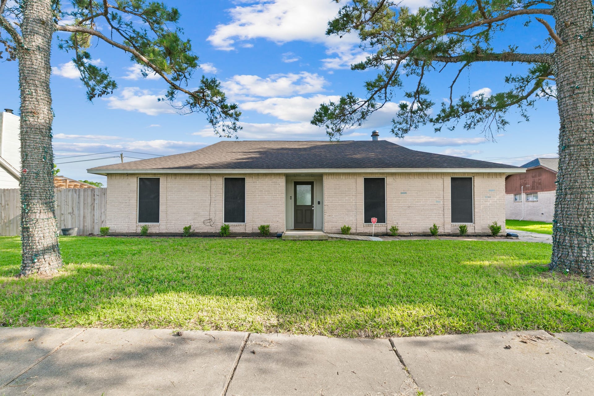 7003 Rockergate Drive, Missouri City, TX 77459 Charming single-story home with a light brick exterior, featuring a neatly maintained lawn and mature trees. The property is set back from the street with a simple, welcoming entrance and a fenced backyard. Ideal for those seeking a cozy, well-kept residence.