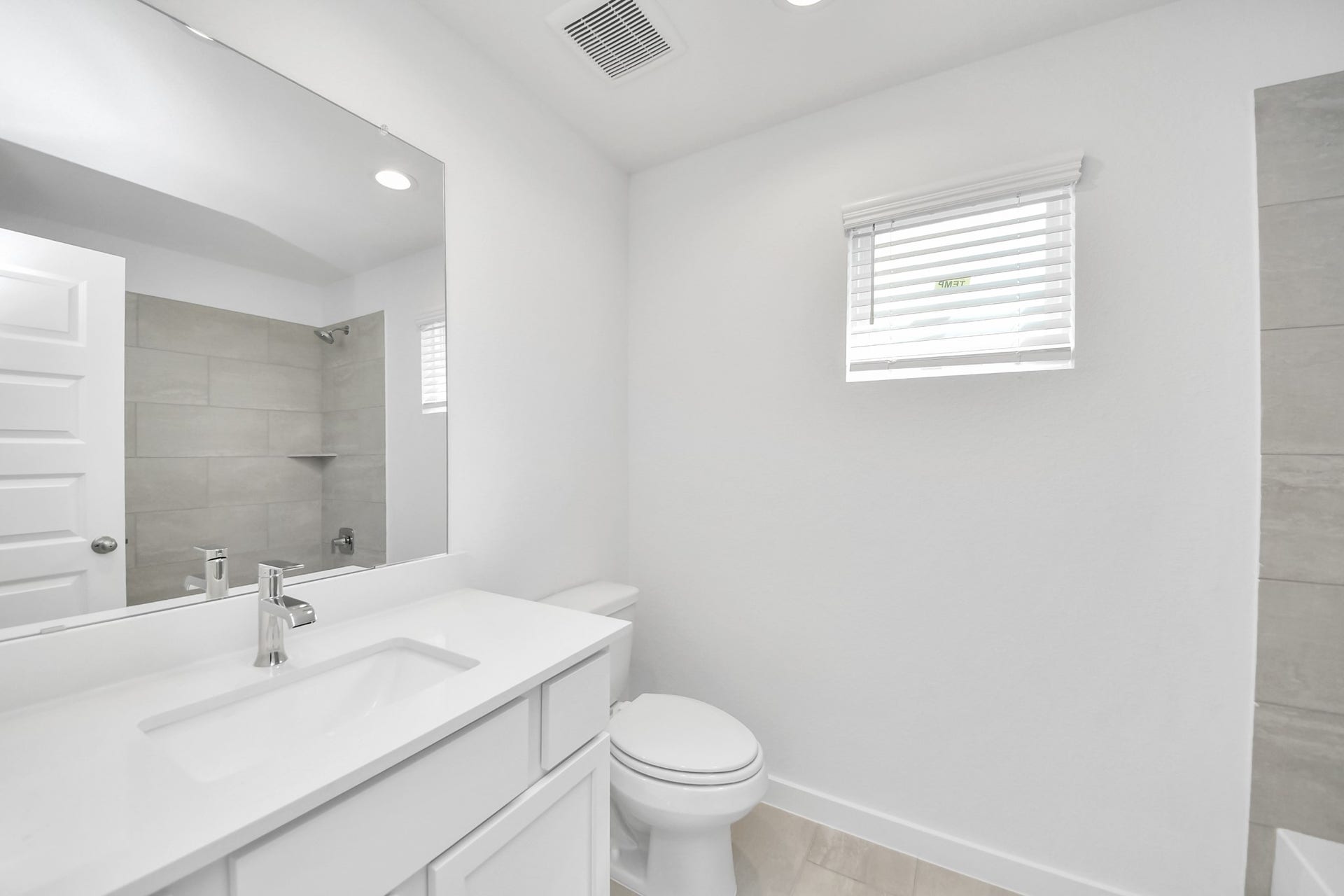 Secondary bath features tile flooring, walk-in shower with tile surround, light stained wood cabinets, beautiful light countertop. Sample photo of completed home with similar floor plan. Actual colors and selections may vary.