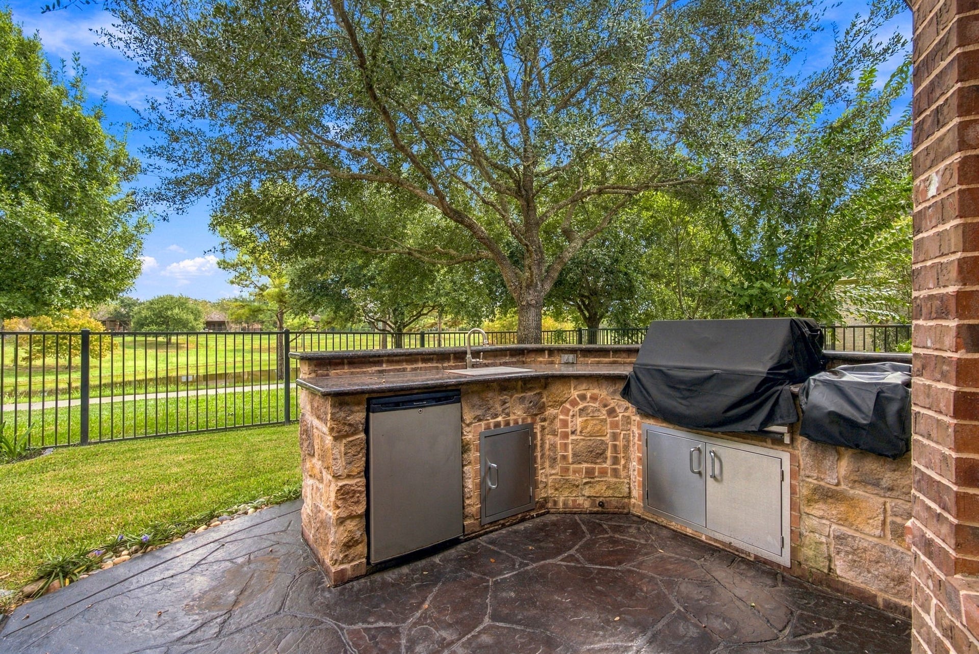 19215 Shady Blossom Drive, Cypress, TX 77433 Amazing outdoor kitchen featuring stone detailing, granite countertops, a built-in grill, a sink, refrigerator, and a griddle.