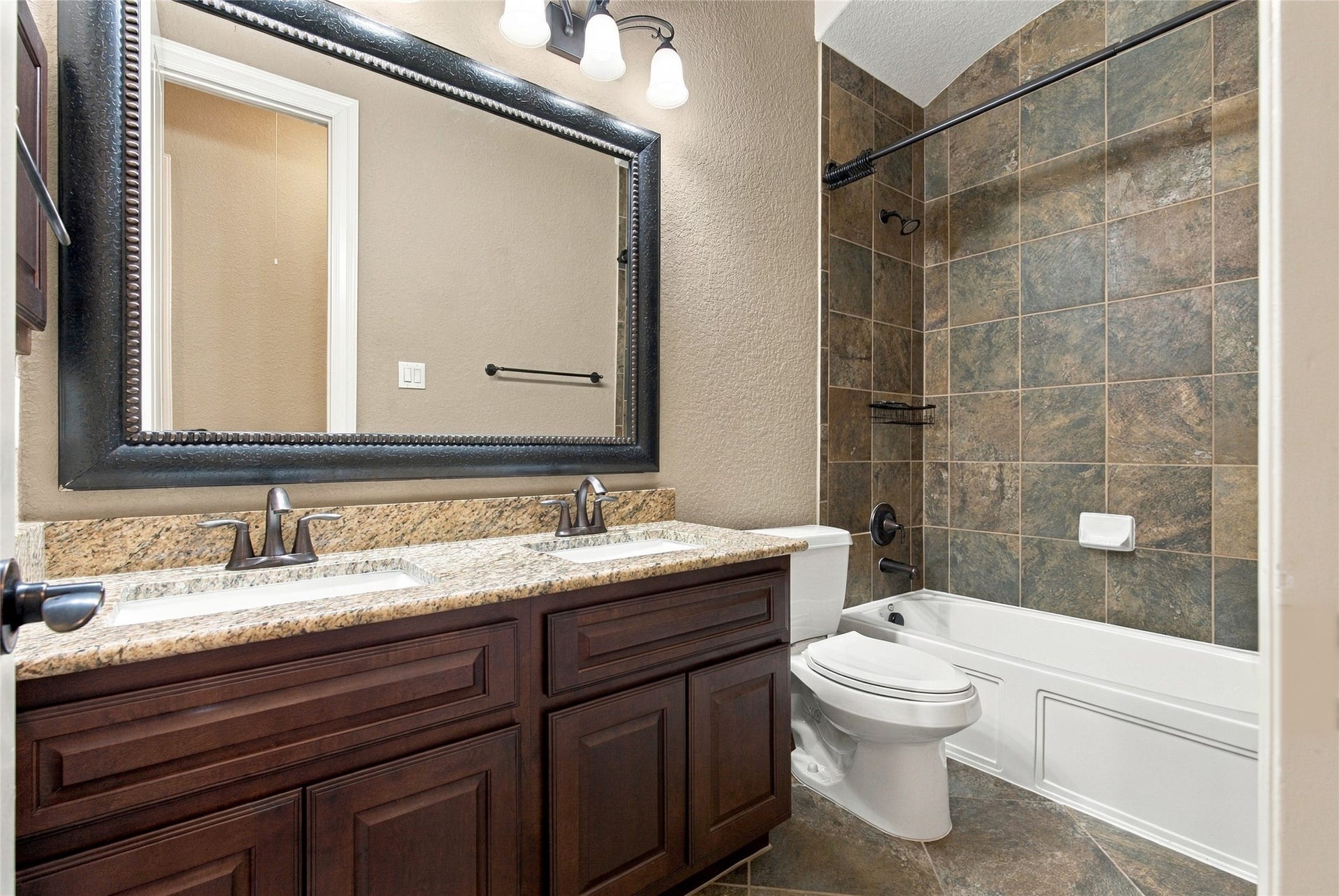 19215 Shady Blossom Drive, Cypress, TX 77433 Full downstairs secondary bathroom featuring a granite countertop, double sinks, framed mirror, and tub/shower combination with decorative tile surround.