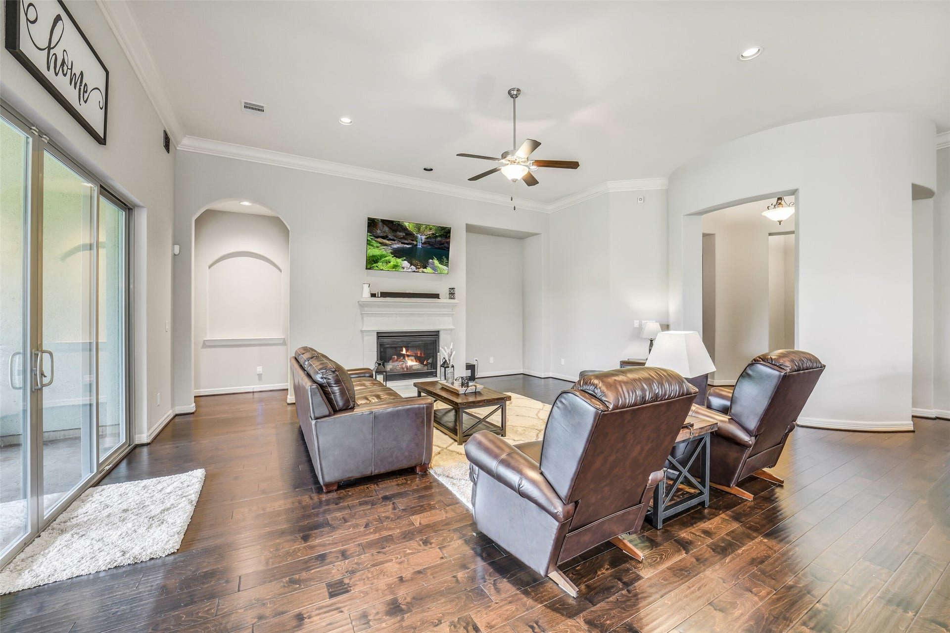 2721 Saddlehorn Trail, Katy, TX 77494 Spacious living room featuring soaring ceilings, rich hardwood floors, a cozy stone fireplace, and oversized sliding doors that fill the space with natural light and provide seamless access to the covered patio.