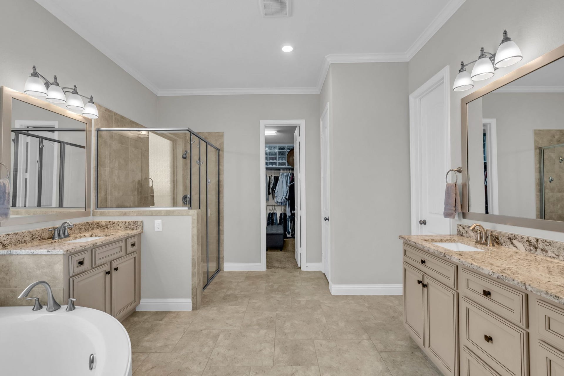 Lavish primary bedroom offers dual vanities, a glass-enclosed shower, a soaking tub, and a massive walk-in closet.