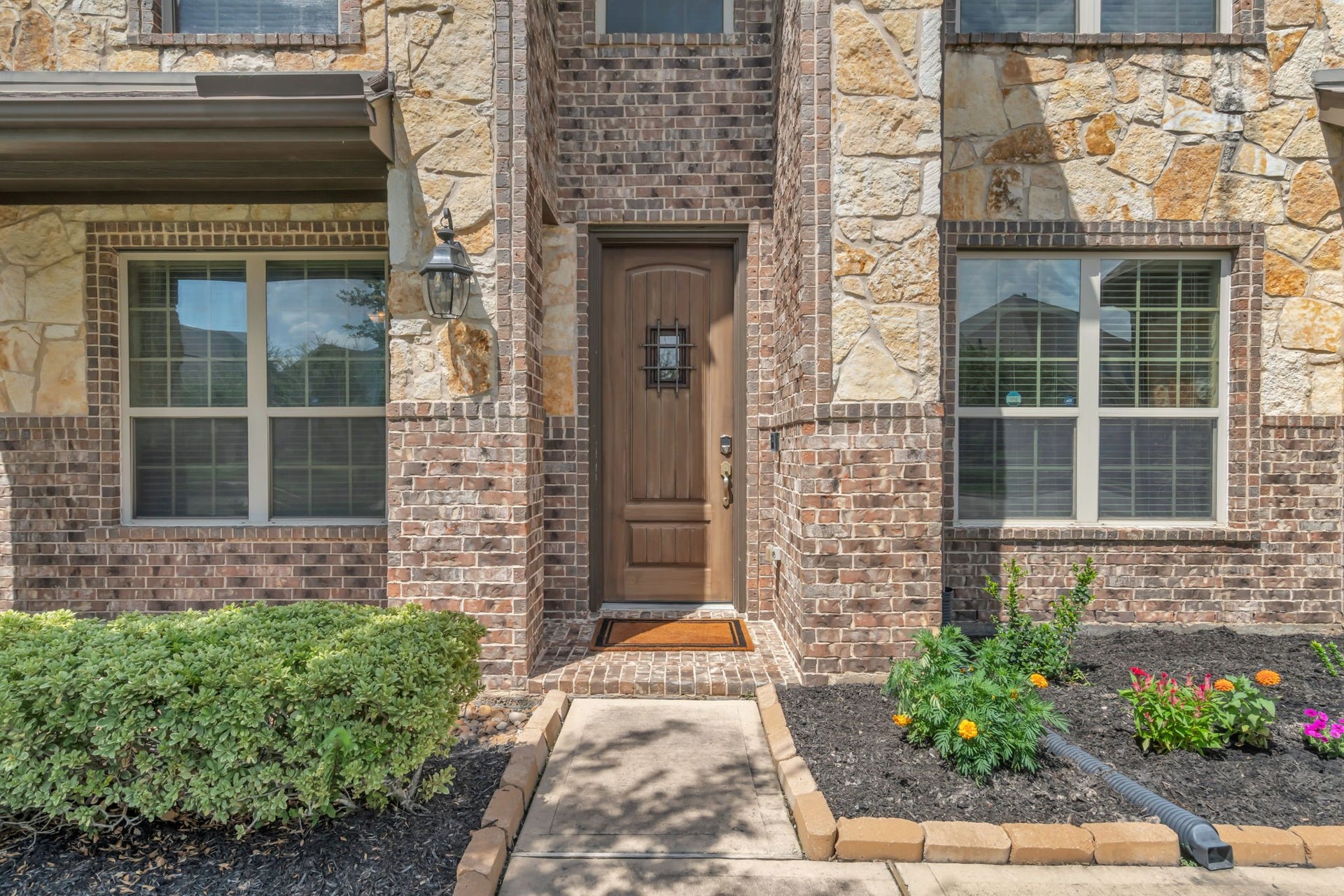 Charming covered porch leads to a warm wood front door surrounded by colorful landscaping.