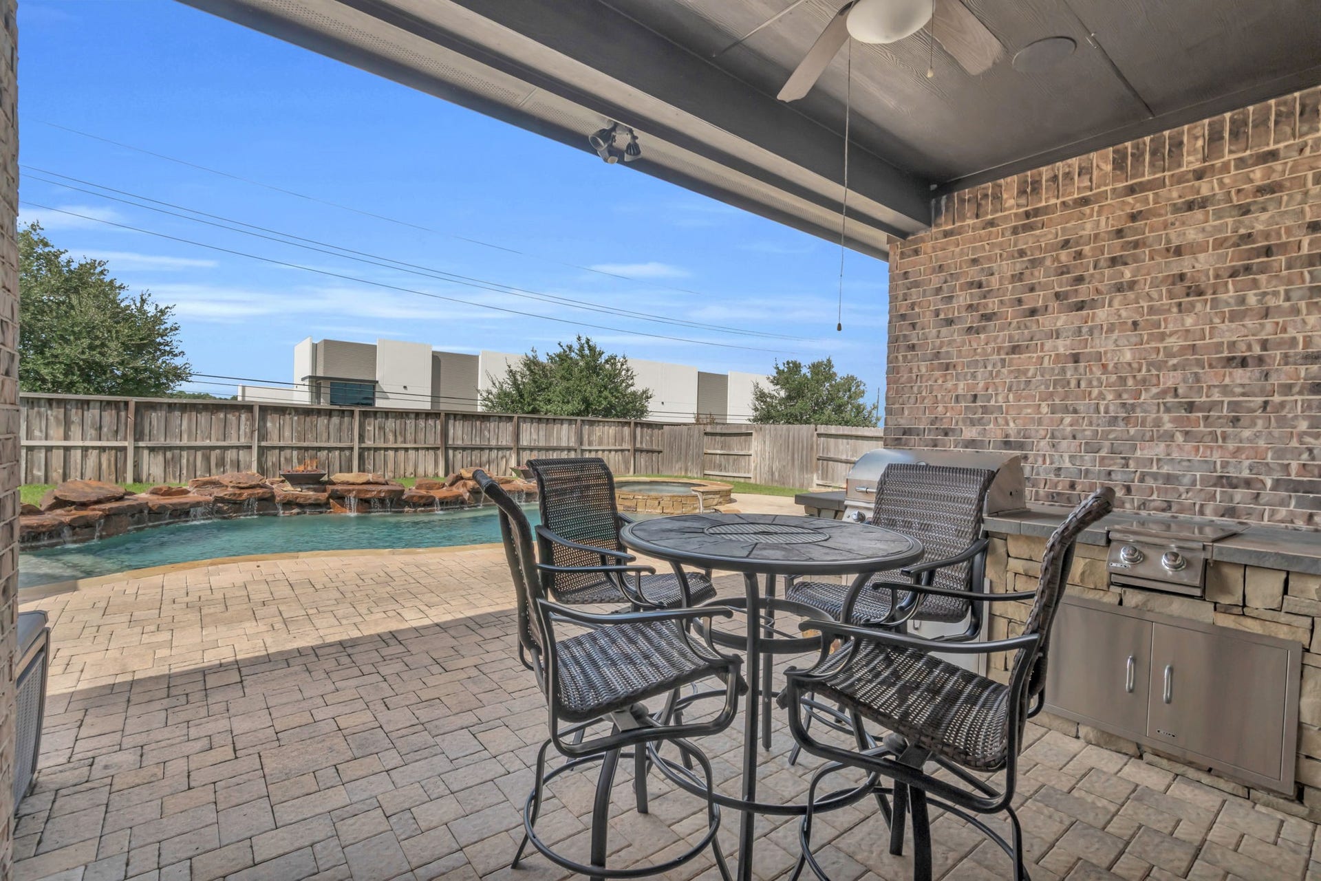 Backyard oasis begins with a large covered patio featuring a built-in grill, a ceiling fan, and a seating area.