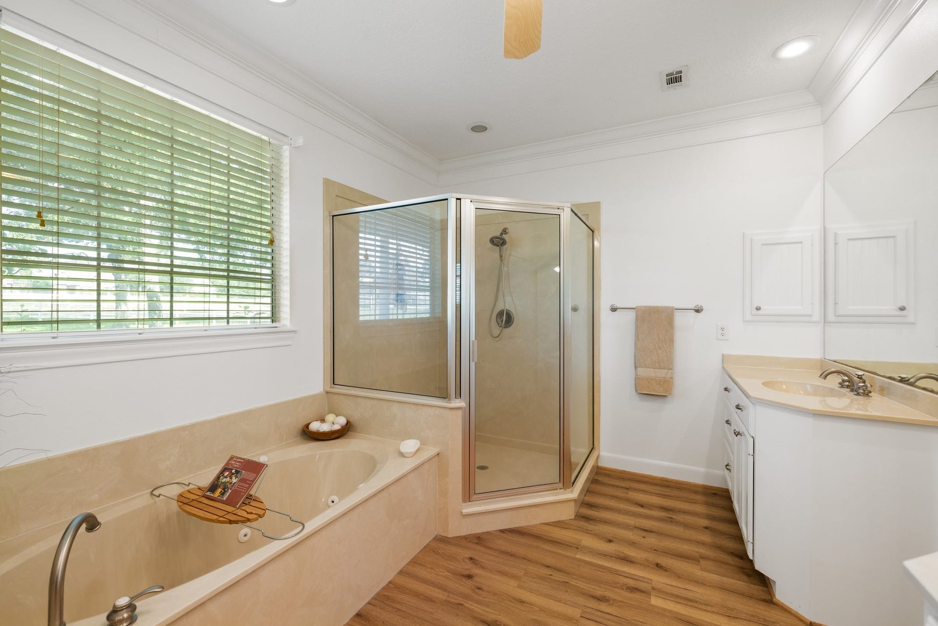 34310 High Point Drive, Magnolia, TX 77355 This bathroom features a spacious layout with a large jetted soaking tub, a separate glass-enclosed shower, and a dual-sink vanity. Natural light streams in through a window with blinds, highlighting the neutral color palette for a modern, inviting atmosphere.