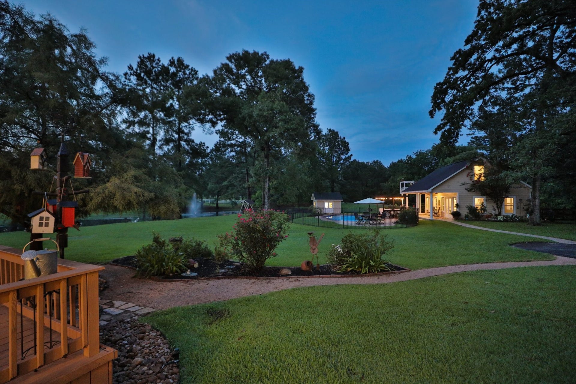 34310 High Point Drive, Magnolia, TX 77355 Stunning sunset view of this serene property features a spacious backyard with lush greenery, a charming pond with a fountain, and a well-lit house. There's a pool area perfect for relaxation or entertaining. The setting feels private and inviting.