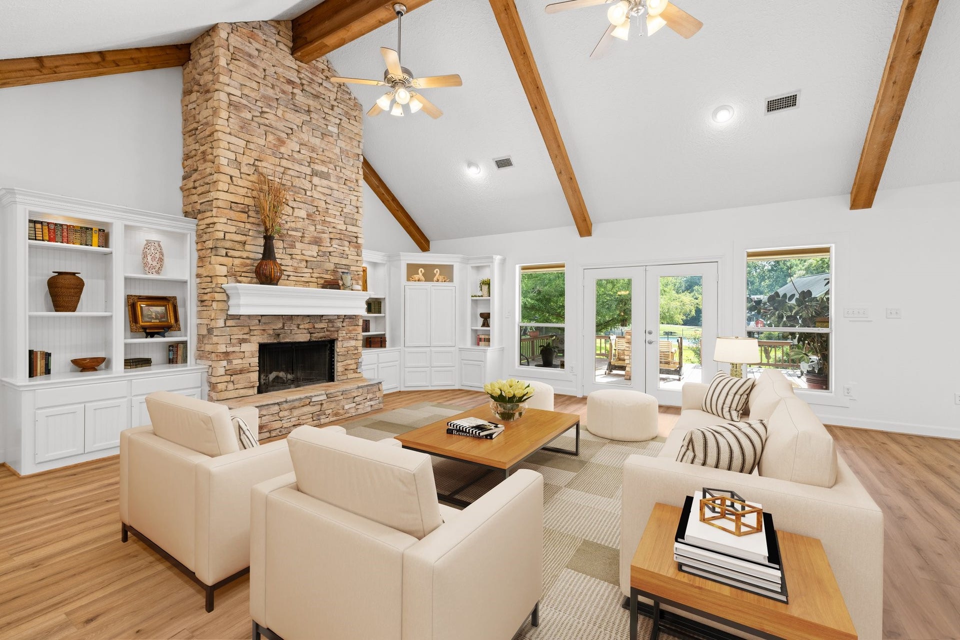 34310 High Point Drive, Magnolia, TX 77355 This spacious living room features a high vaulted ceiling with exposed wooden beams, a striking stone fireplace, and built-in shelving. Large windows and French doors offer plenty of natural light and views of the outdoor greenery.