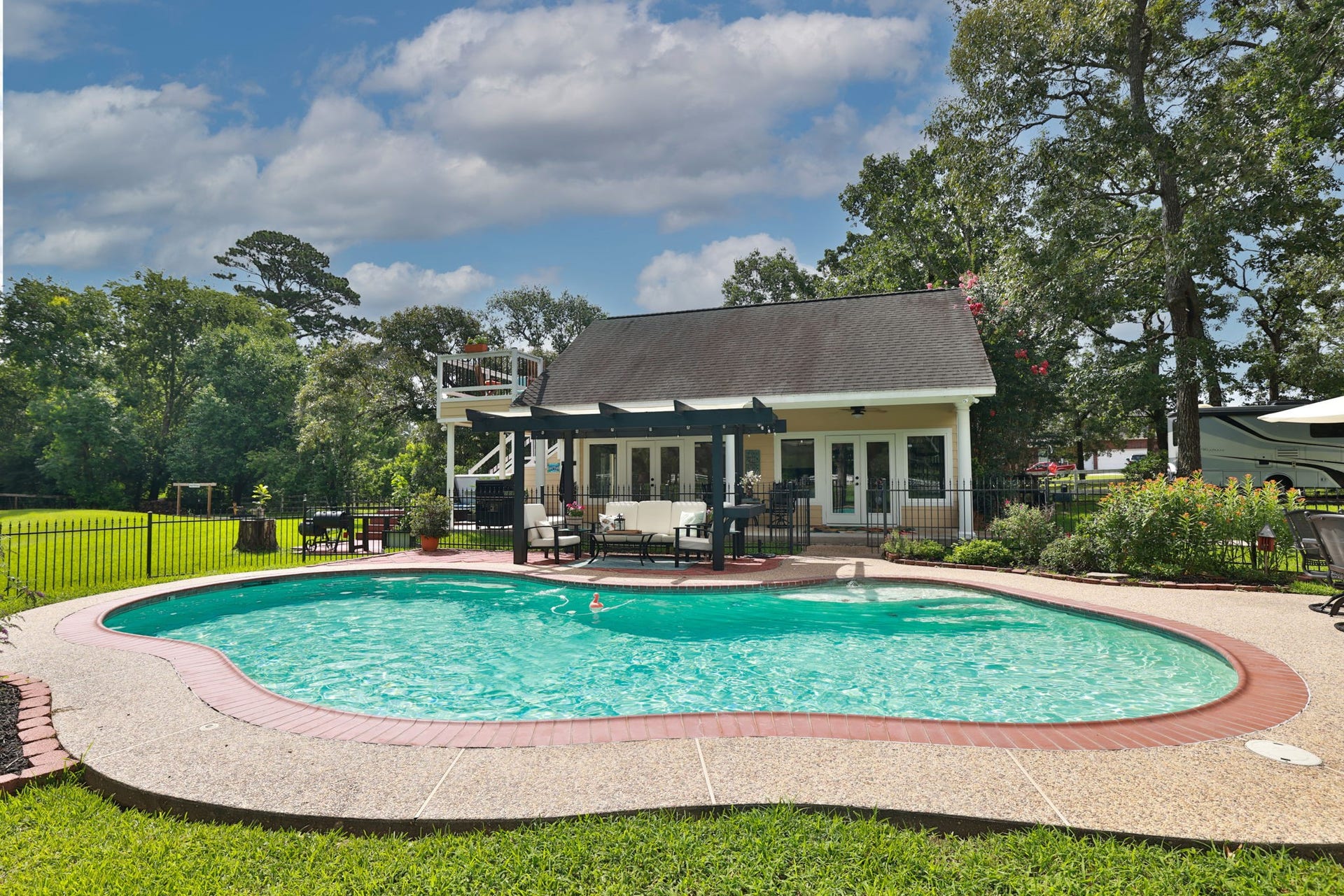 34310 High Point Drive, Magnolia, TX 77355 This photo showcases a charming backyard with a kidney-shaped pool, surrounded by a well-maintained lawn and a cozy patio area. The guest house has a rustic design with a pergola for outdoor relaxation, and mature trees provide shade and privacy. Ideal for summer entertaining.