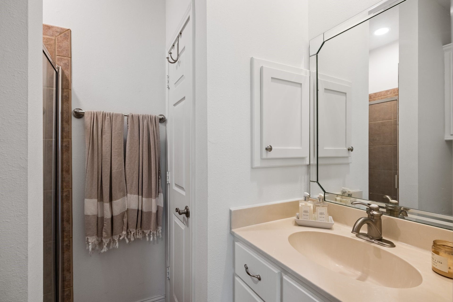 34310 High Point Drive, Magnolia, TX 77355 This bathroom features a modern design with a tiled shower, cream countertop, and a stylish mirror. It includes white cabinetry and a towel rack, providing a clean and functional space.