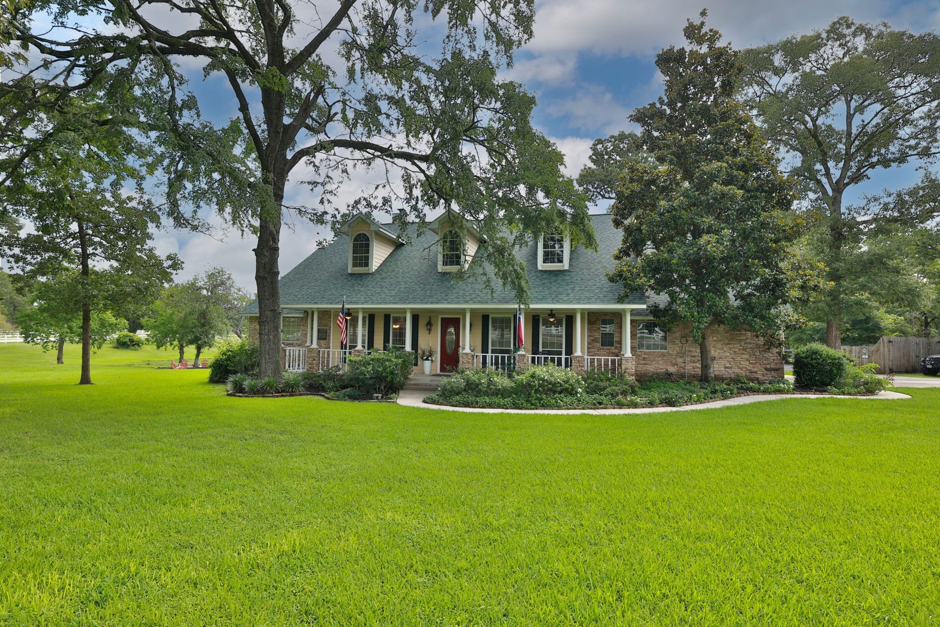 34310 High Point Drive, Magnolia, TX 77355 Charming two-story home with a classic front porch, nestled among mature trees and lush green lawn. Perfect for peaceful living with ample outdoor space.
