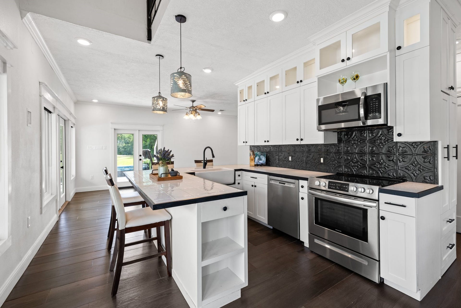 34310 High Point Drive, Magnolia, TX 77355 This modern kitchen fin the guest house features sleek white cabinetry with glass accents, stainless steel appliances, and a stylish black tile backsplash. The open layout includes a cozy breakfast bar, contemporary pendant lighting, and offers a spacious view to the outdoors through glass doors, creating a bright and inviting space.
