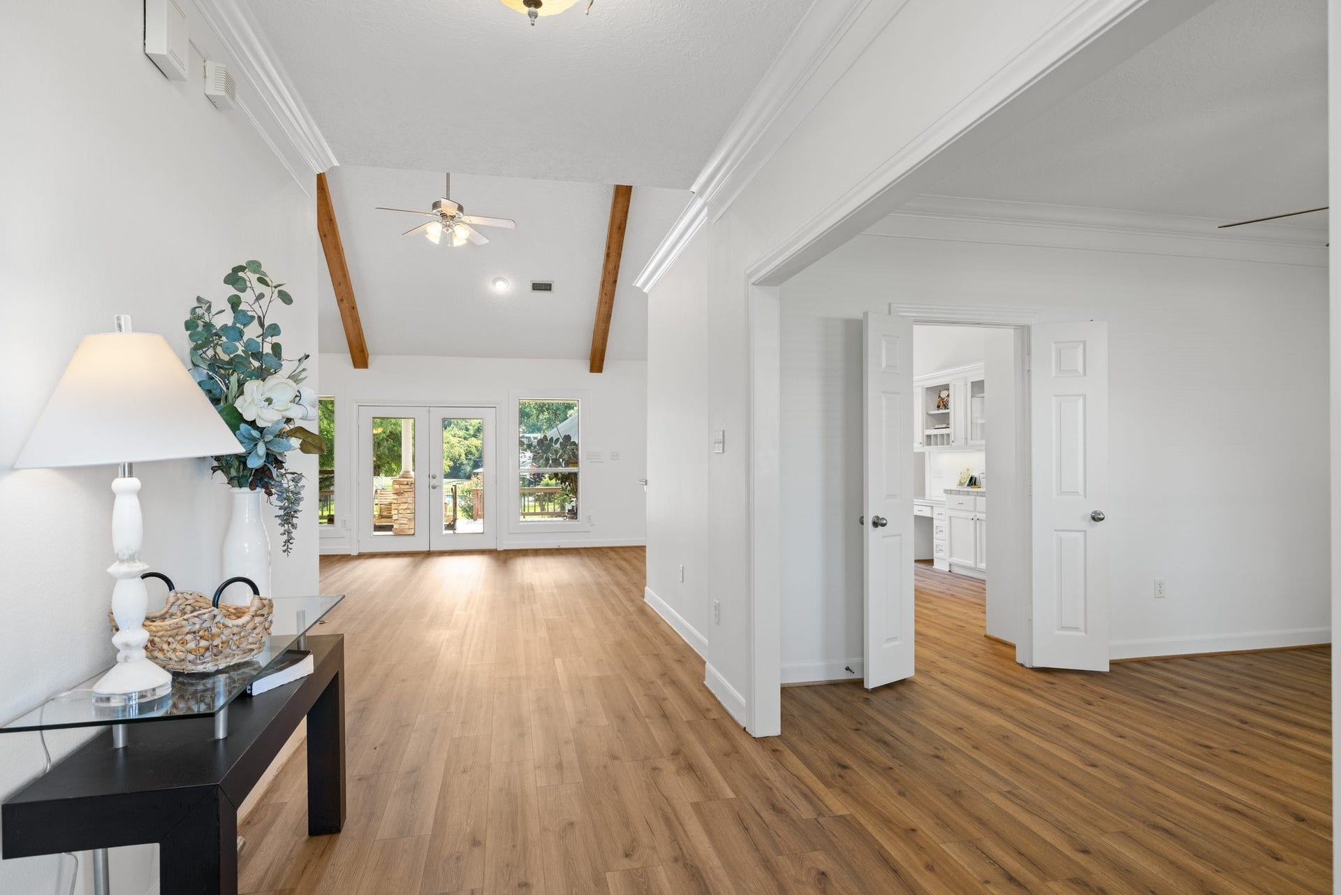 34310 High Point Drive, Magnolia, TX 77355 Bright and inviting entryway with vaulted ceilings and exposed beams. The open floor plan features vinyl plank flooring and leads to a spacious living area with glass doors opening to a backyard view.