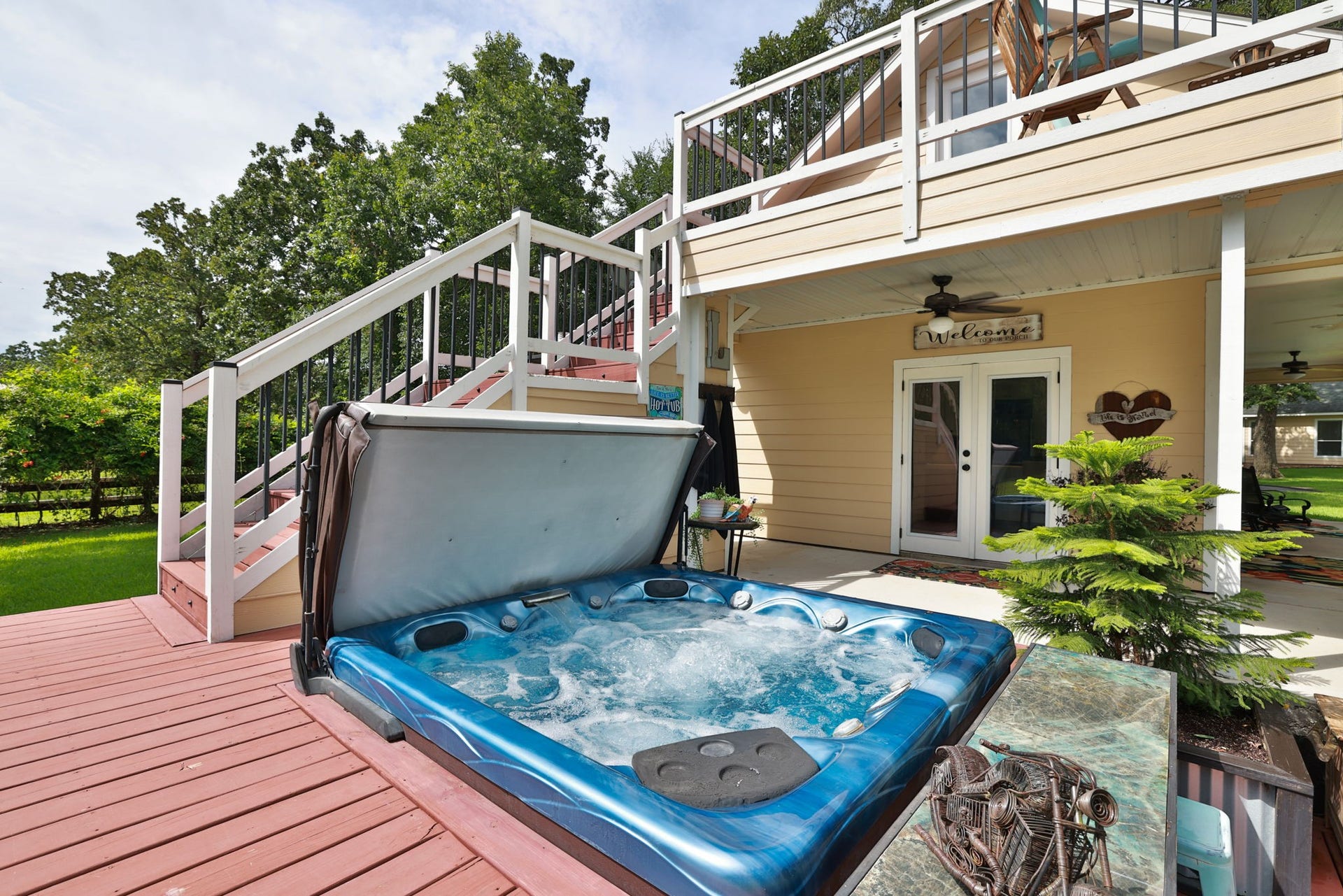 34310 High Point Drive, Magnolia, TX 77355 This inviting outdoor space features a bubbling hot tub on a spacious deck, leading up to a cozy balcony. The area is complemented by a charming covered patio with ceiling fans, perfect for relaxation and entertaining. Lush greenery surrounds the setting, adding to the serene atmosphere.