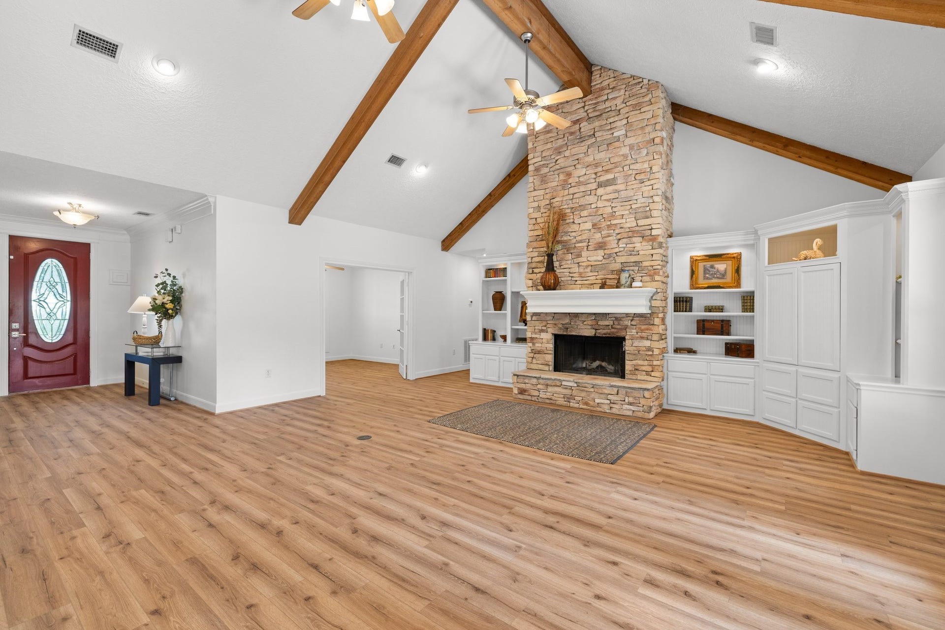 34310 High Point Drive, Magnolia, TX 77355 This spacious living room features a high vaulted ceiling with exposed wood beams, a beautiful floor to ceiling stone fireplace, and built-in shelving. The open layout and natural light create a warm, inviting atmosphere, complemented by vinyl plank flooring and a stylish entry door.