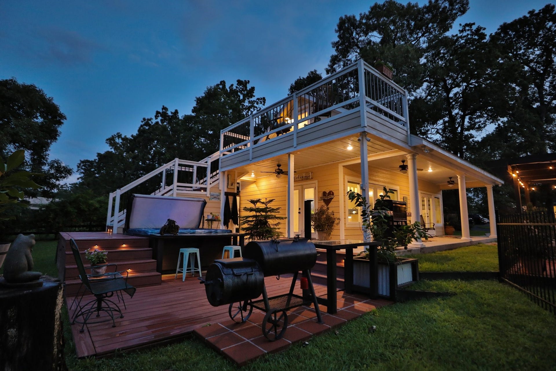 34310 High Point Drive, Magnolia, TX 77355 Inviting sunset view of the 1,000 guest home features a spacious two-level deck with ample outdoor seating, a hot tub, and a grill area, perfect for entertaining. The well-lit patio and surrounding greenery create a cozy ambiance for evening gatherings.