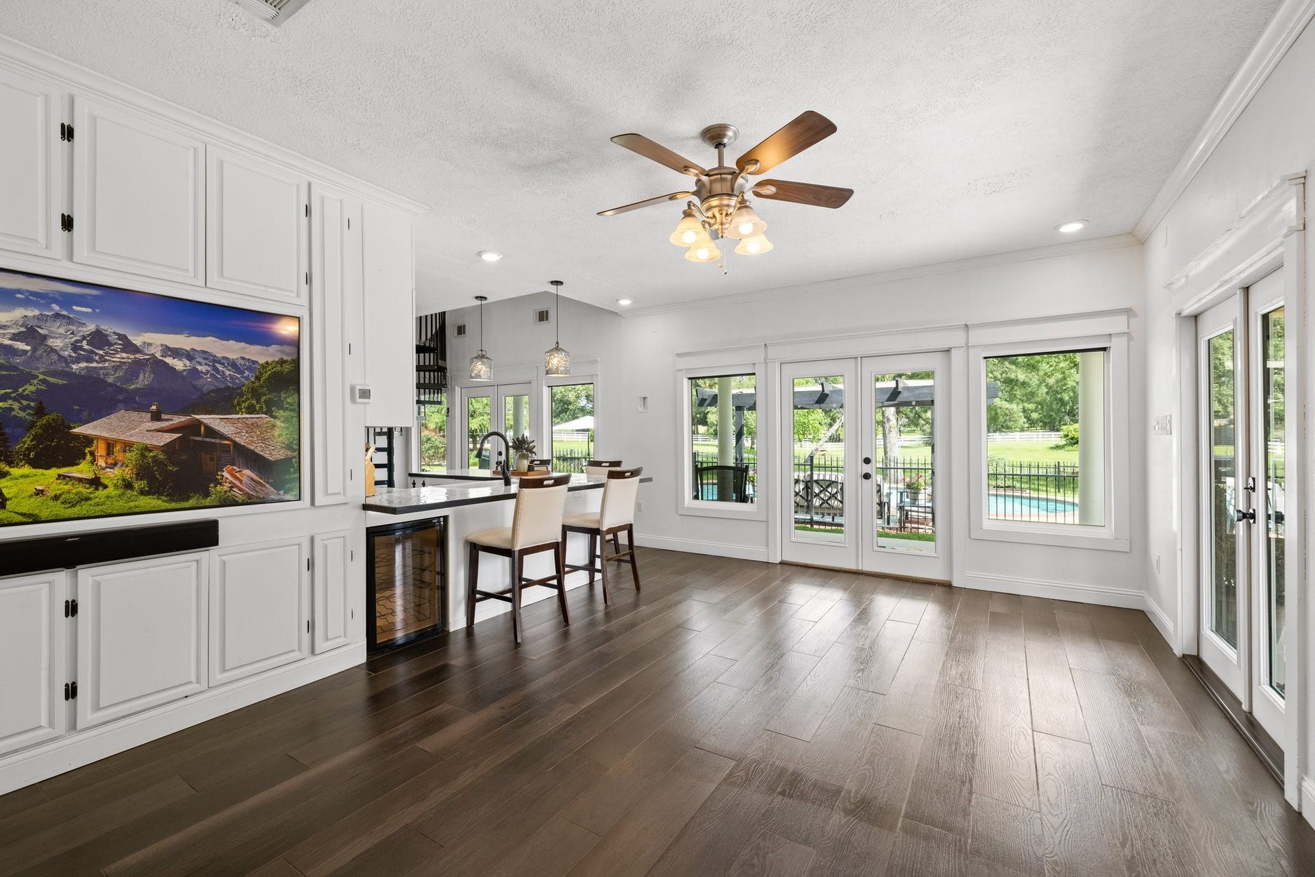 34310 High Point Drive, Magnolia, TX 77355 This spacious, bright living room in the guest house features elegant tile wood look floors and a ceiling fan. It opens to a scenic backyard with large windows and French doors, offering views of a pool and greenery. The open concept includes a modern kitchen with a breakfast bar and stylish lighting.
