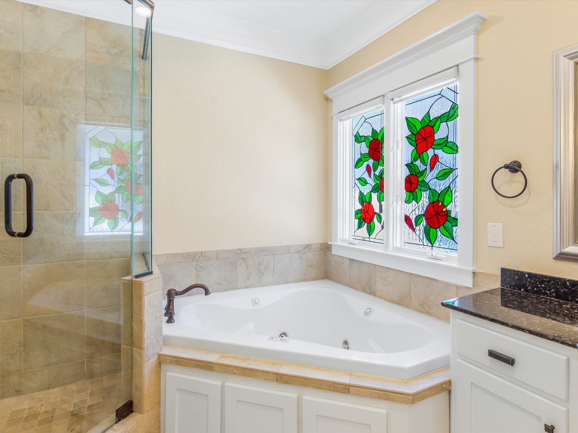 837 E 27th Street, Houston, TX 77009 Elegant bathroom featuring a luxurious corner jetted bathtub with charming stained glass windows, complemented by a spacious glass-enclosed shower and sleek countertops.